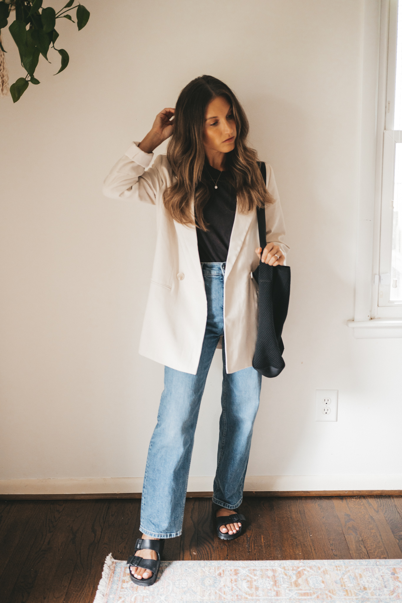 ashley wearing a black tee, beige oversized blazer, mid-wash straight denim, black plastic Birkenstocks, and a black tote bag