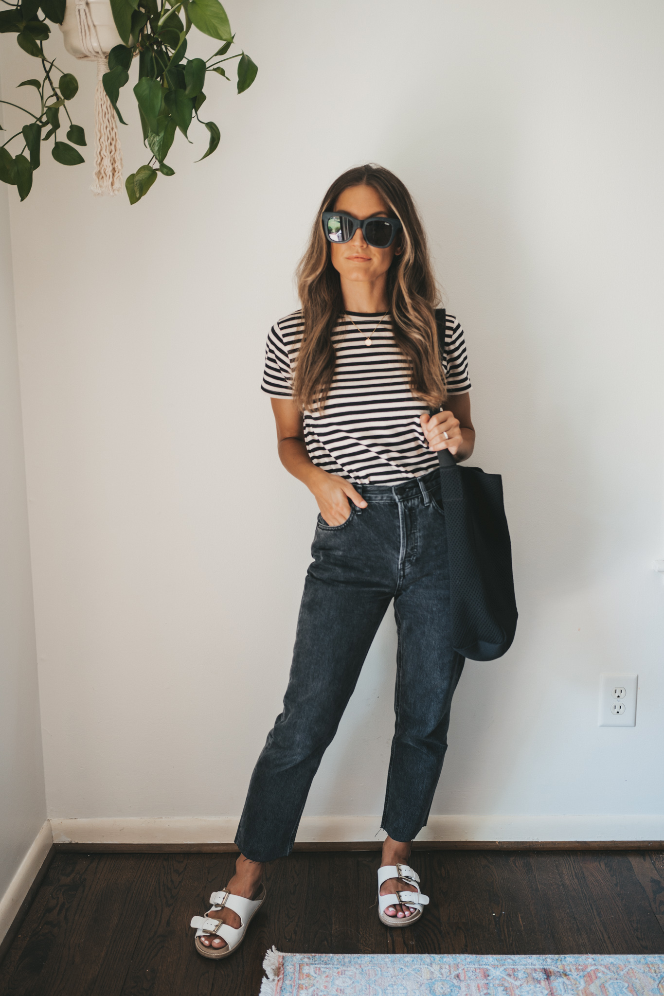 ashley wearing a white and black striped tee, washed black straight denim, white footbed sandals, and a black tote bag