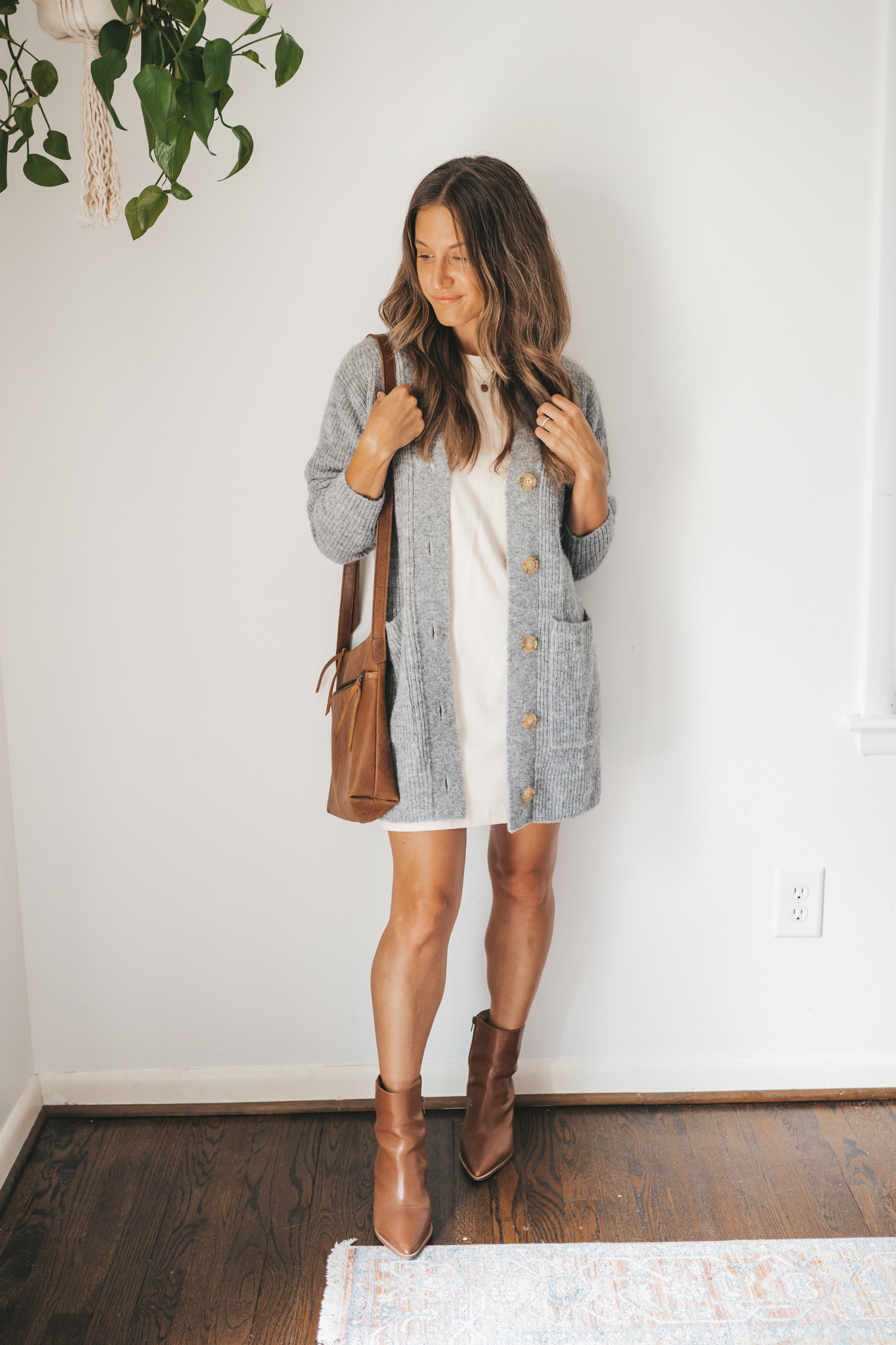 ashley wearing a cream colored t-shirt dress, gray long line cardigan, and cognac ankle boots with a cognac cross body bag