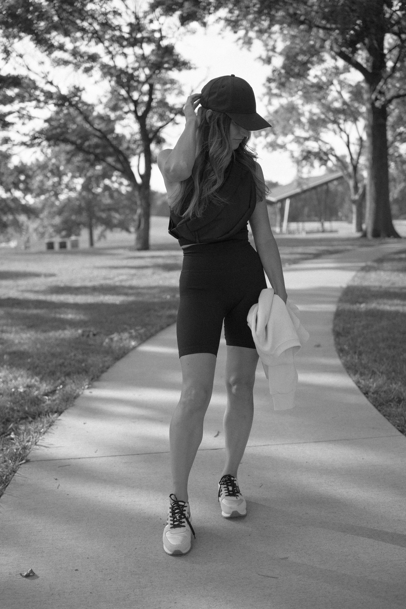 a black and white photo of ashley wearing a black ribbed tank and black ribbed biker shorts with sneakers standing on a path in a park