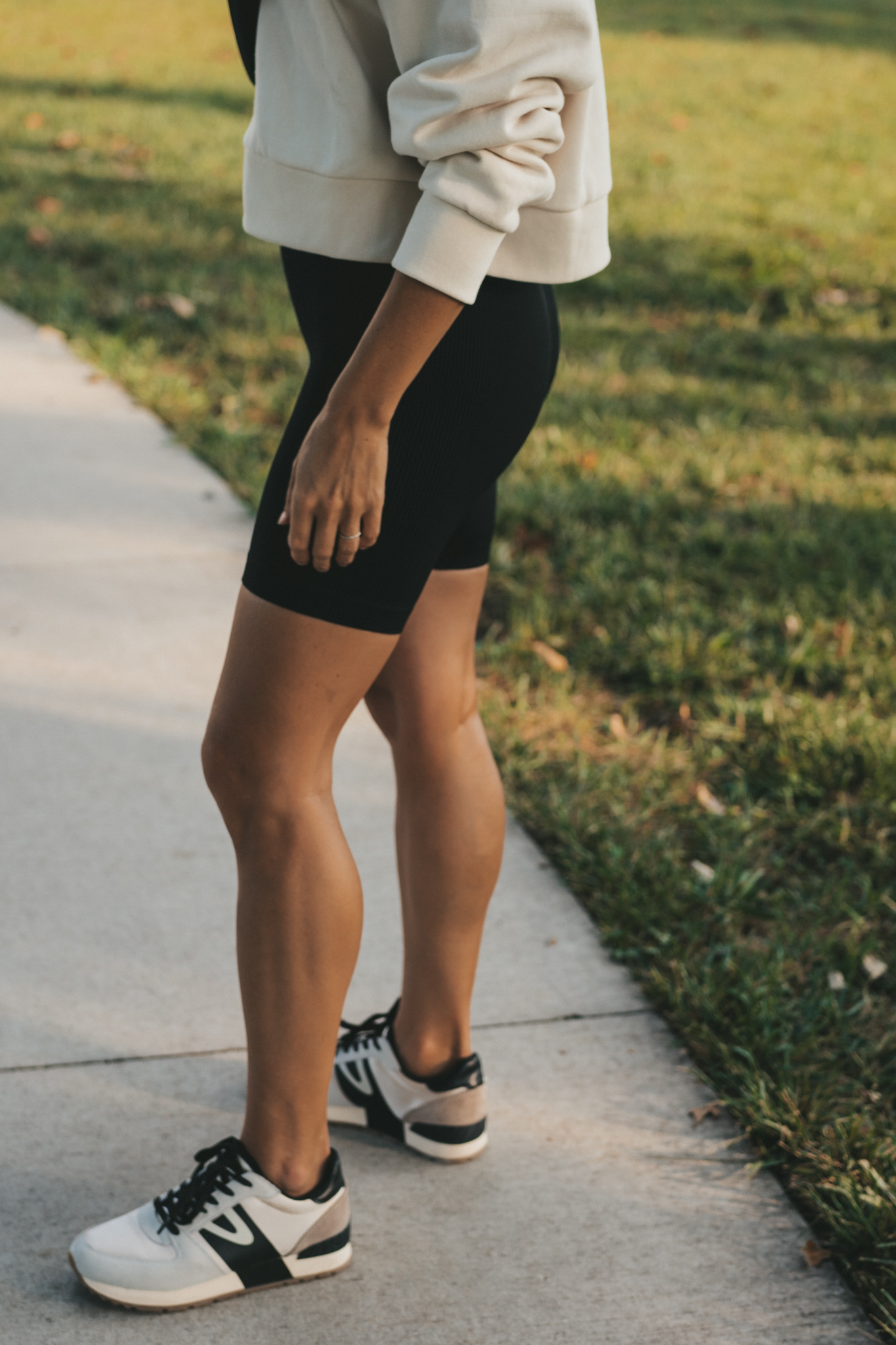 athleisure outfit idea with black biker shorts, a cropped cream colored sweatshirt, and casual sneakers
