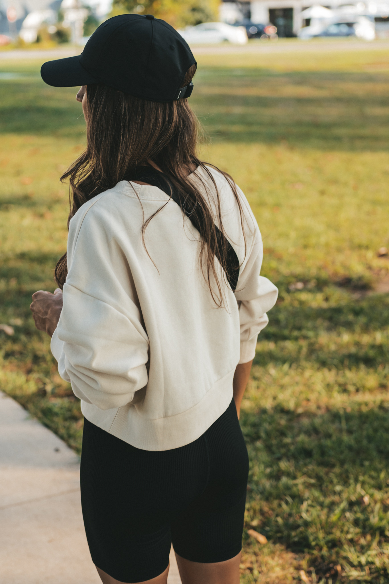 ashley wearing a cream colored cropped tank, black ribbed biker shorts, a black belt bag, and a black baseball cap