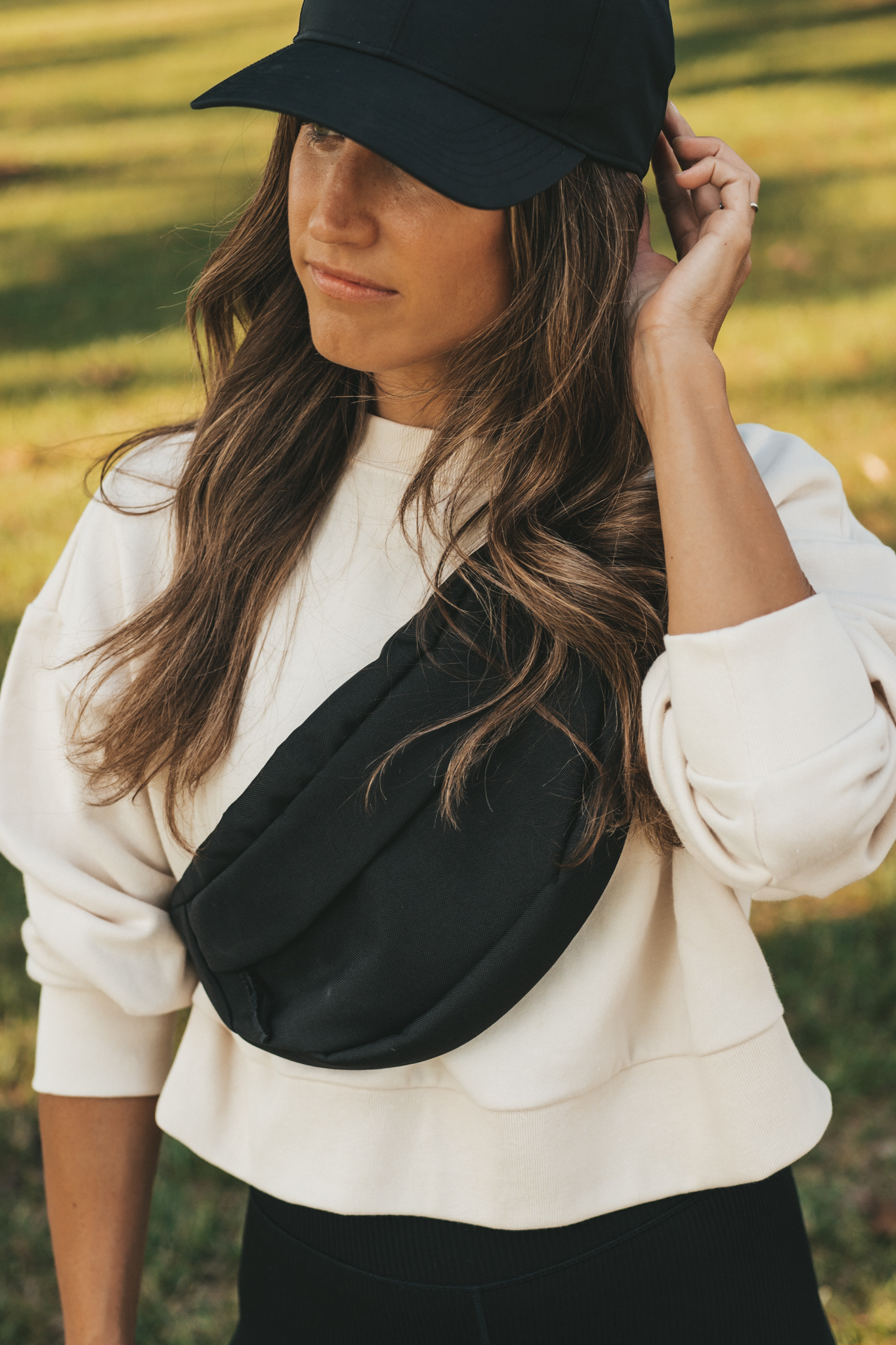 ashley wearing a cream colored cropped tank, black ribbed biker shorts, a black belt bag, and a black baseball cap