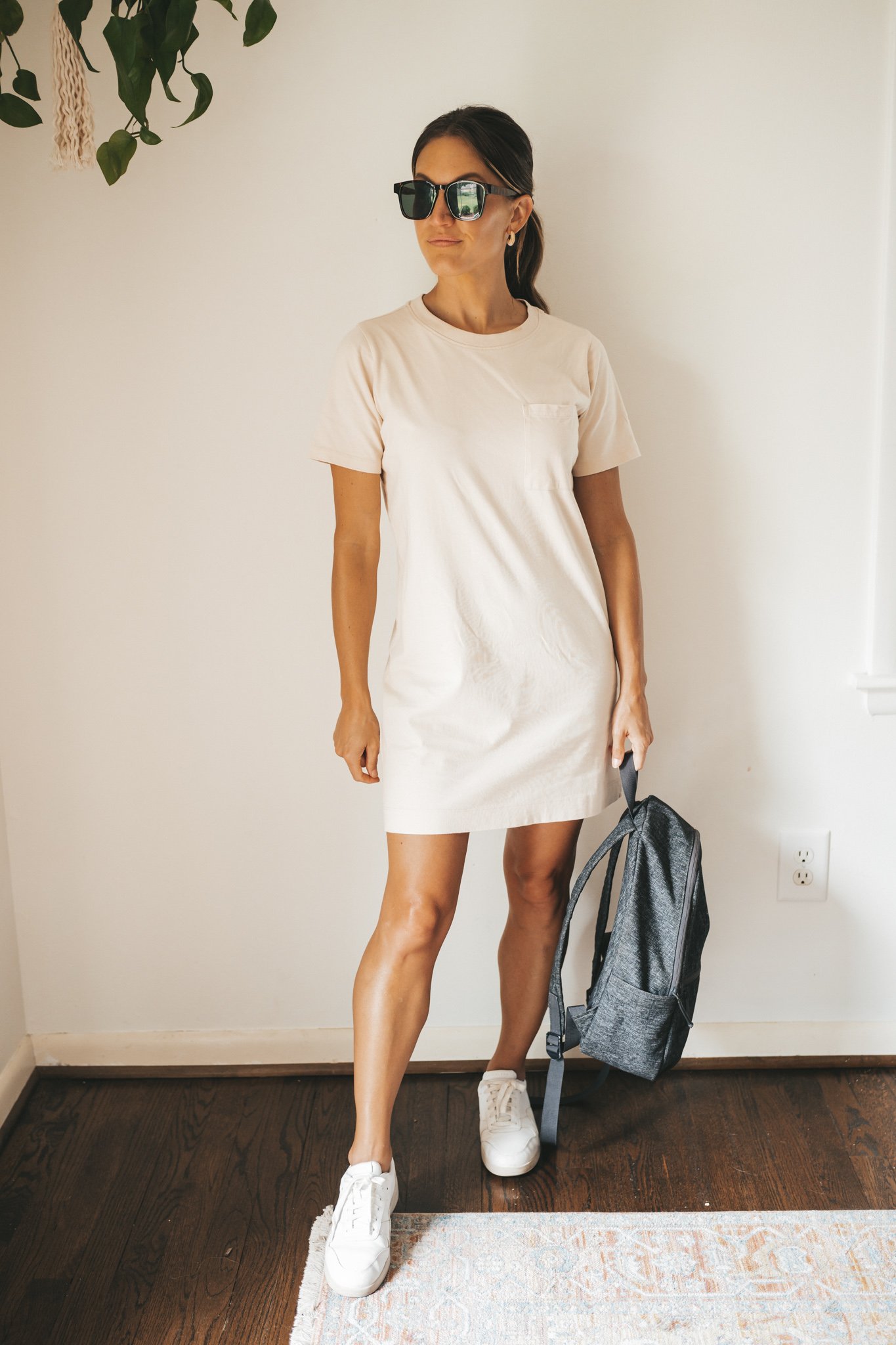 ashley wearing a cream colored t-shirt dress, white sneakers, and a dark gray backpack