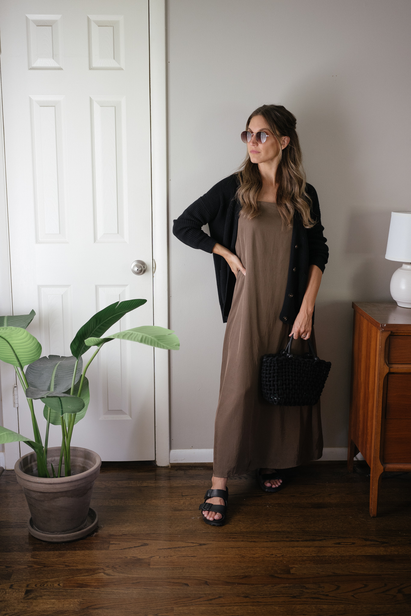transitional outfit idea with a green slip dress, black cardigan, and black Birkenstocks