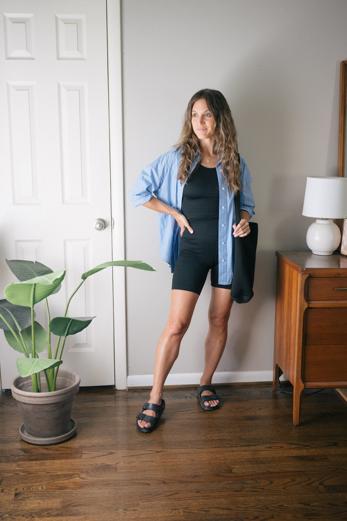transitional outfit idea with a black ribbed tank, black ribbed biker shorts, and an oversized blue striped button down with black Birkenstocks