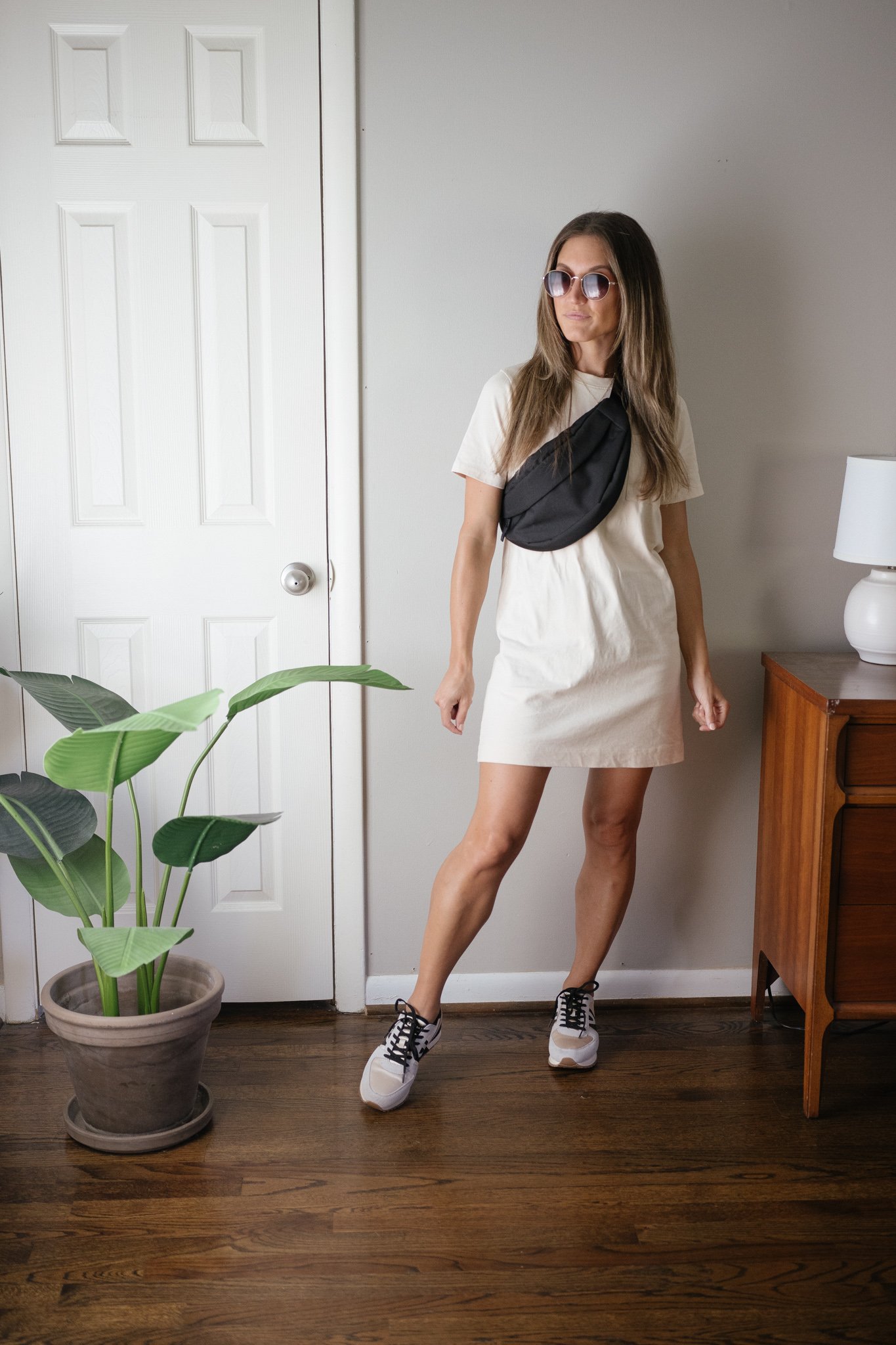 transitional outfit idea with a cream colored t-shirt dress, black belt bag, and casual colorblock sneakers