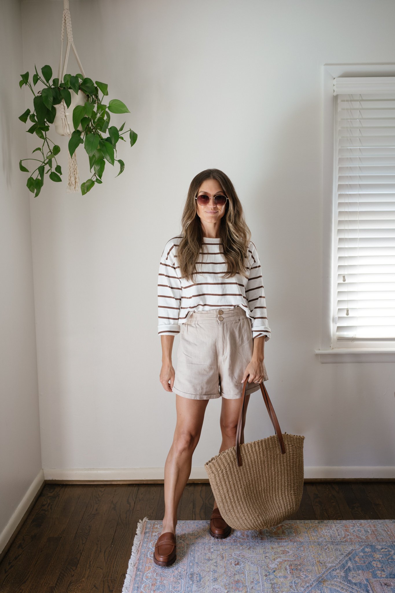 ashley wearing a long sleeved striped tee, tan linen shorts, brown loafer mules, and a woven tote bag