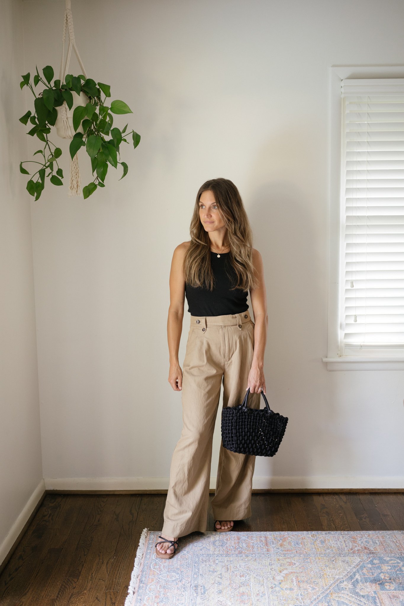 ashley wearing a black tank, wide leg trousers, strappy black sandals, and a black woven bag