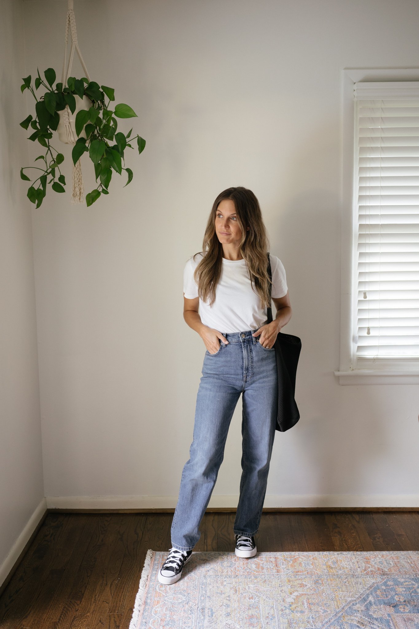 ashley wearing a white tee, mid-wash straight denim, black high top Converse, and a black tote bag