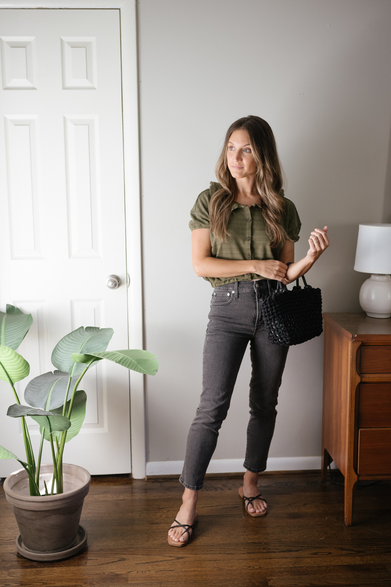 transitional outfit idea with a green blouse, black denim, black strappy sandals, and a black woven bag