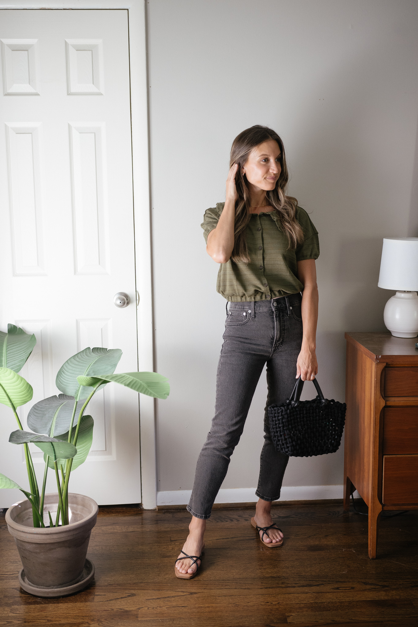 transitional outfit idea with a green blouse, black denim, black strappy sandals, and a black woven bag