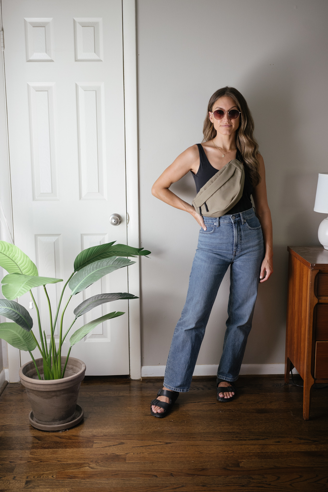 transitional outfit with a black bodysuit, straight leg denim, black Birkenstocks, and an olive green belt bag