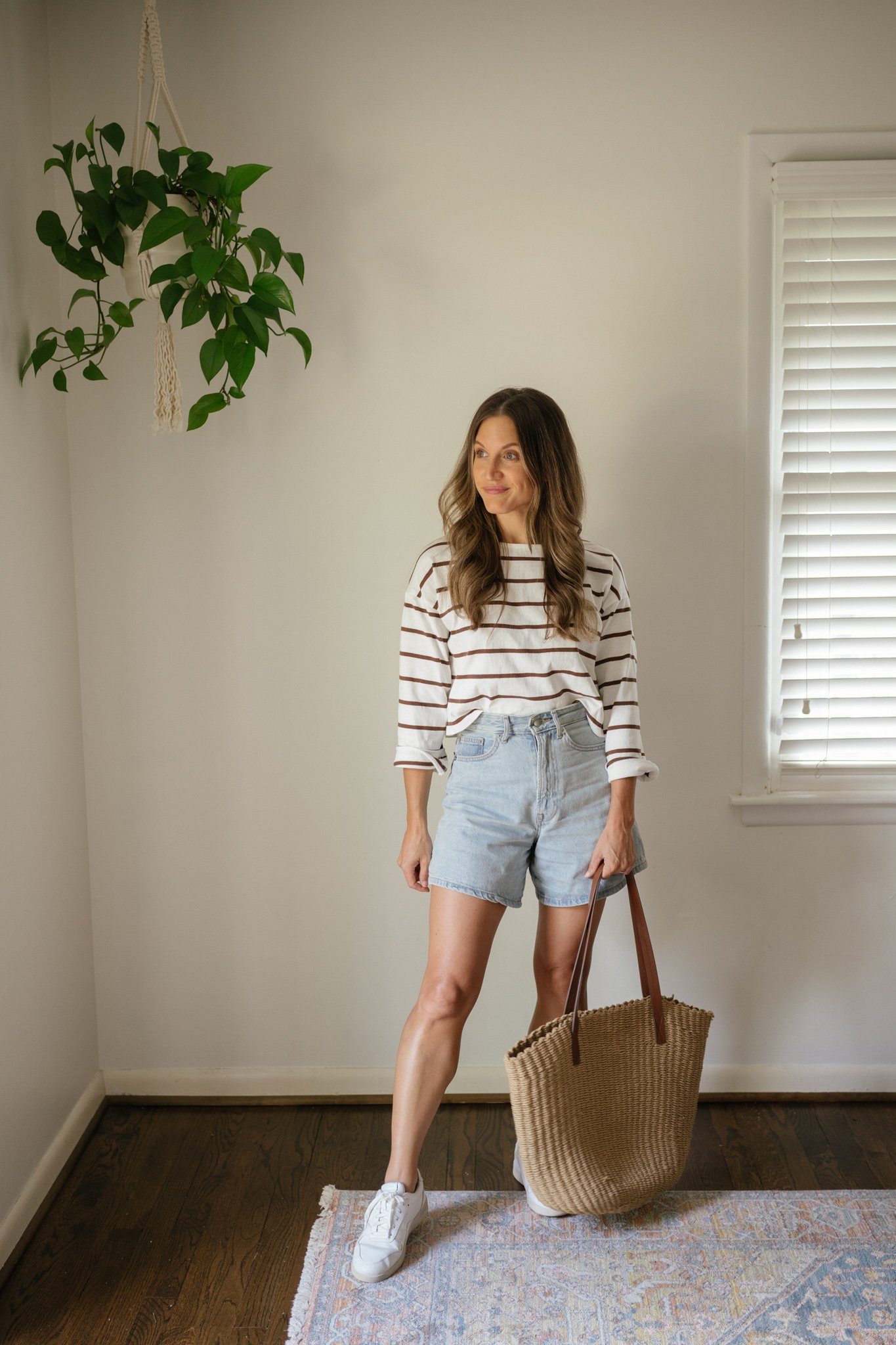 outfit idea for Seattle in the summer with a striped top, light wash denim shorts, white sneakers, and a straw tote bag