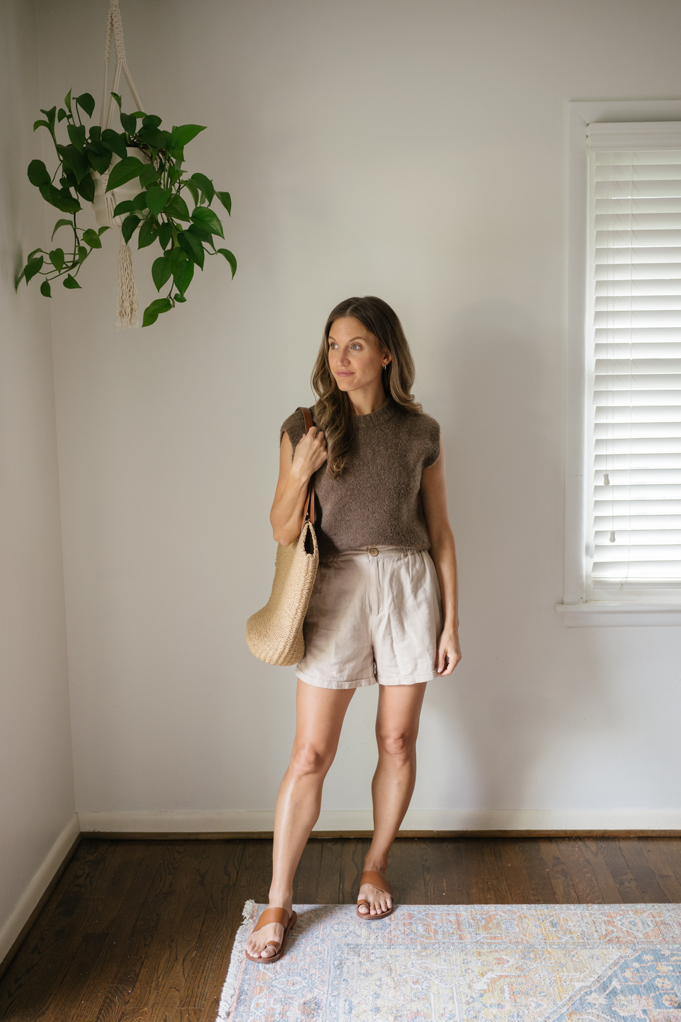 outfit idea for Seattle in the summer with a chocolate brown sweater vest, tan linen shorts, brown leather toe ring sandals, and a straw tote bag