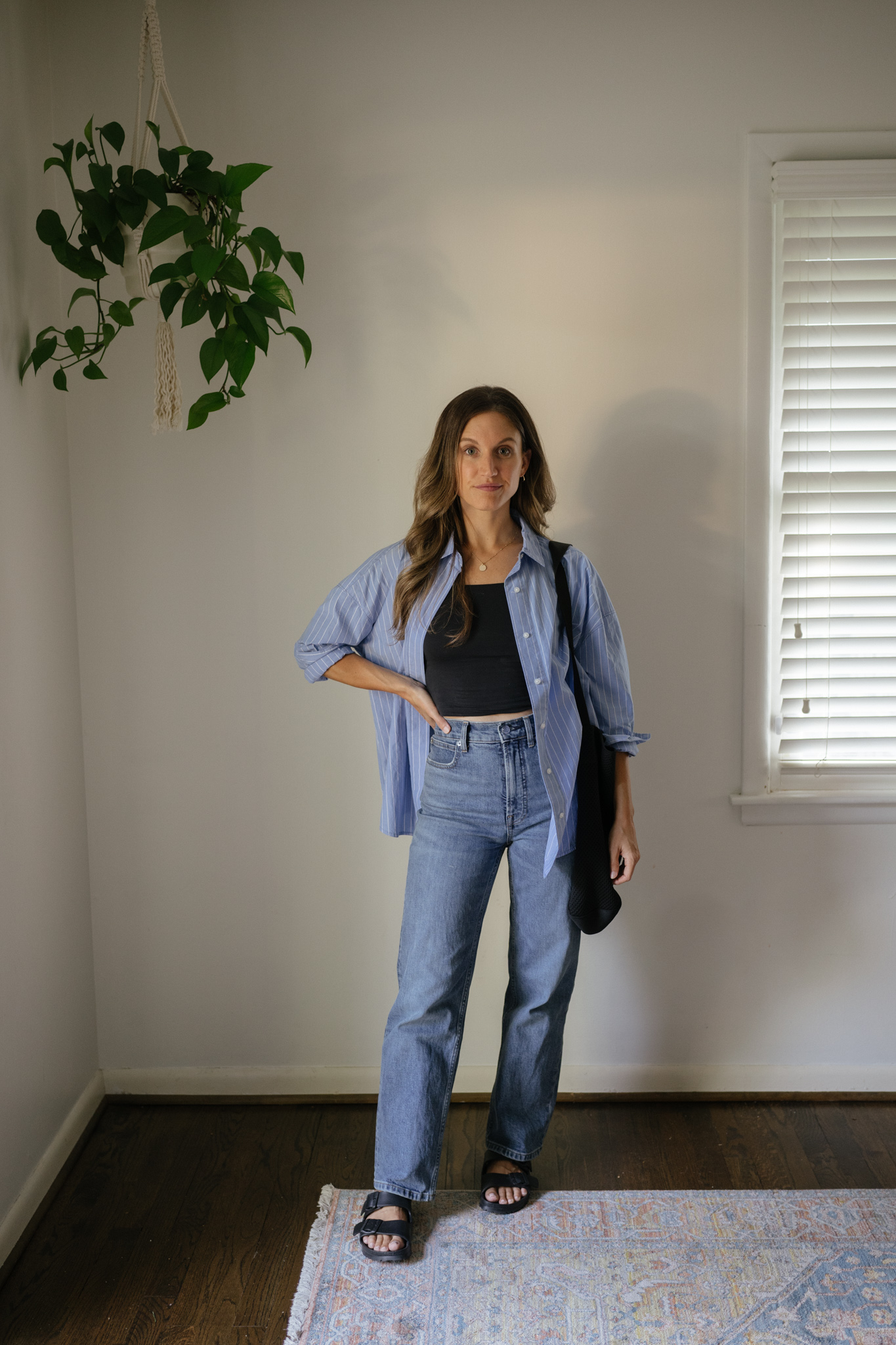 outfit idea for Seattle in the summer with a black cropped tank, a blue and white striped button down worn open, mid-wash straight denim, and black Birkenstocks