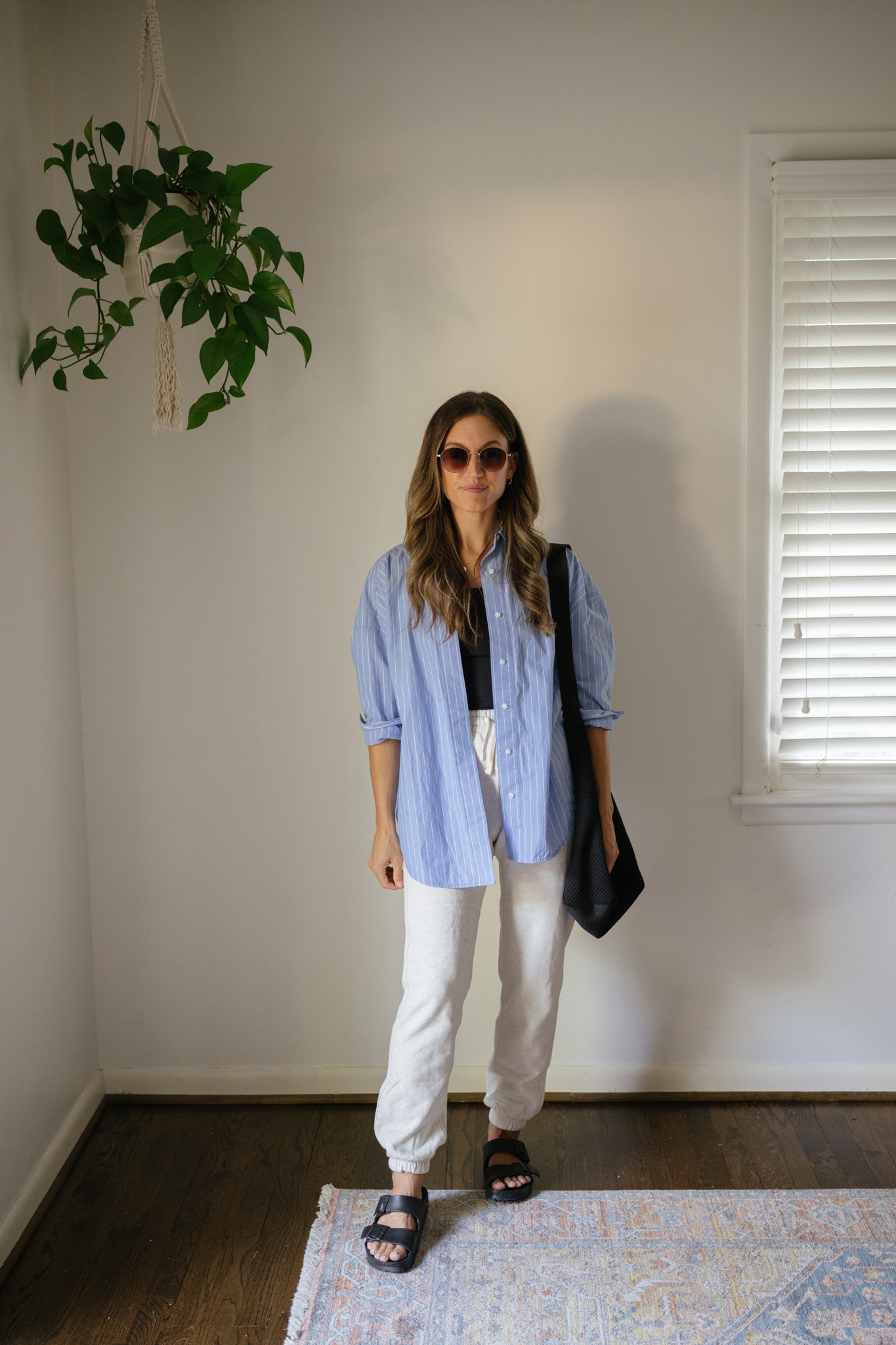 outfit idea for Seattle in the summer with a black cropped tank, a blue and white striped button down worn open, light gray joggers, black Birkenstocks, and a black tote bag