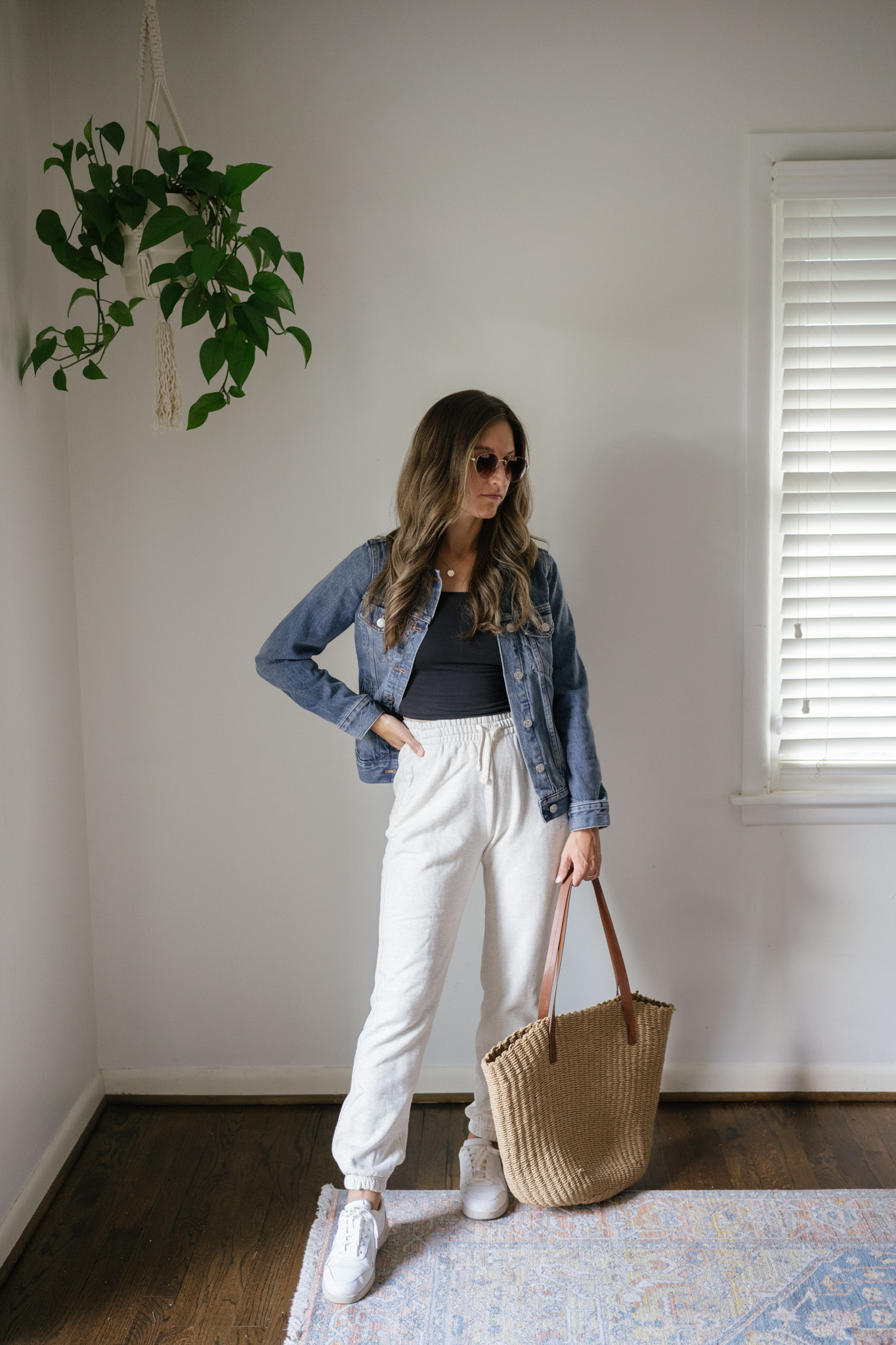 outfit idea for Seattle in the summer with a black cropped tank, denim jacket, light gray joggers, white sneakers, and a woven tote bag