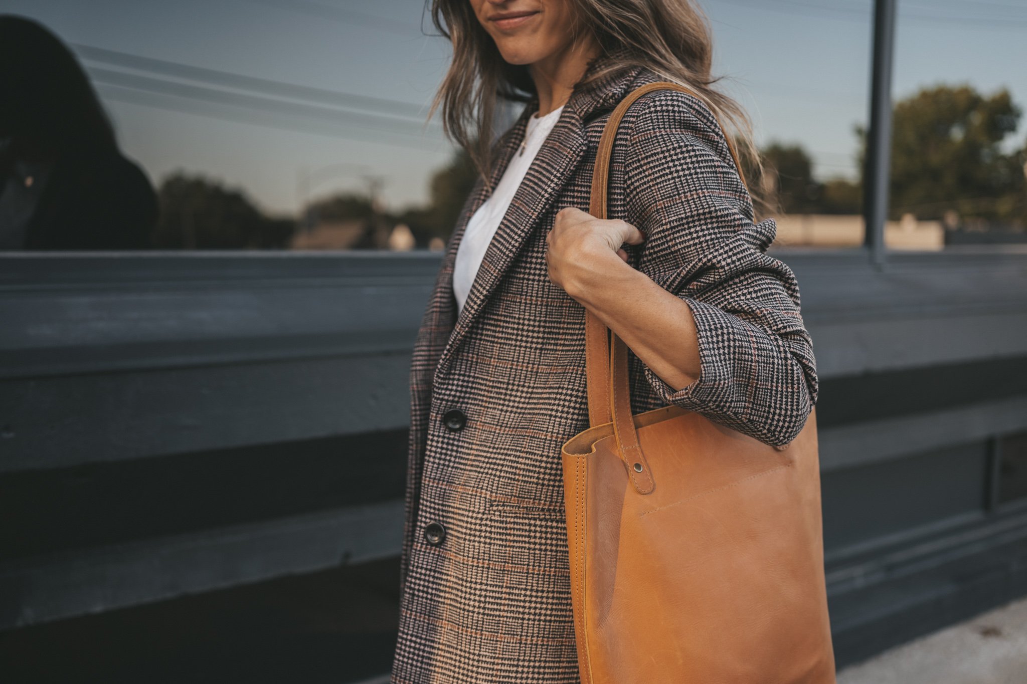 a plaid blazer outfit with a white tee, straight denim, brown ankle boots, and a cognac leather tote bag