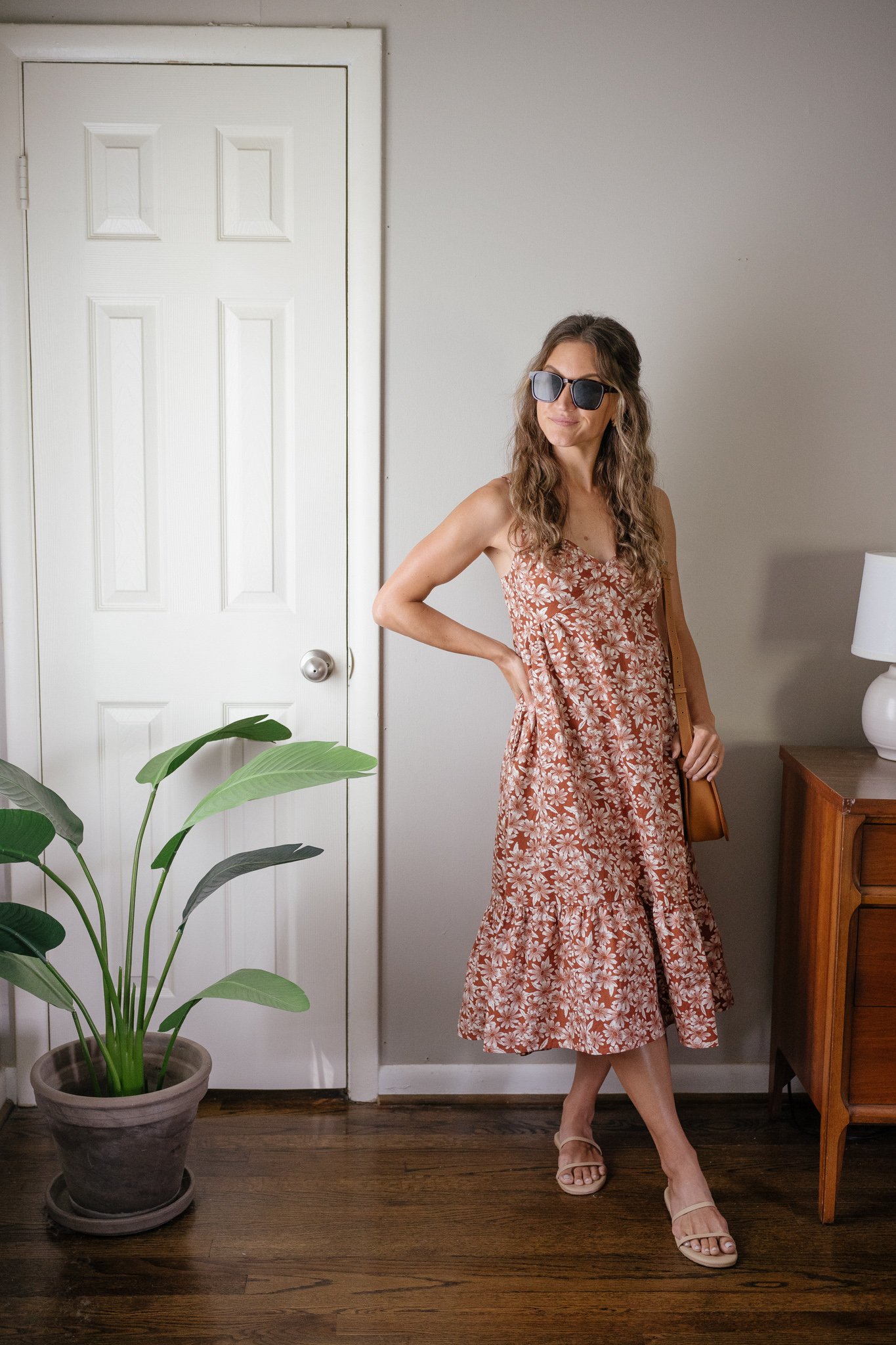 ashley wearing a dark orange floral midi dress with a tiered skirt, nude strappy sandals, a cognac crossbody and tortoise shell sunglasses