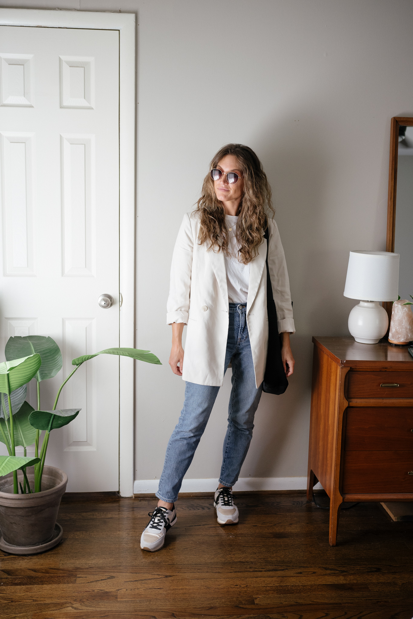 ashley wearing a white tank, beige oversized blazer, mid-wash straight denim, neutral colorblock casual sneakers, and a black tote bag