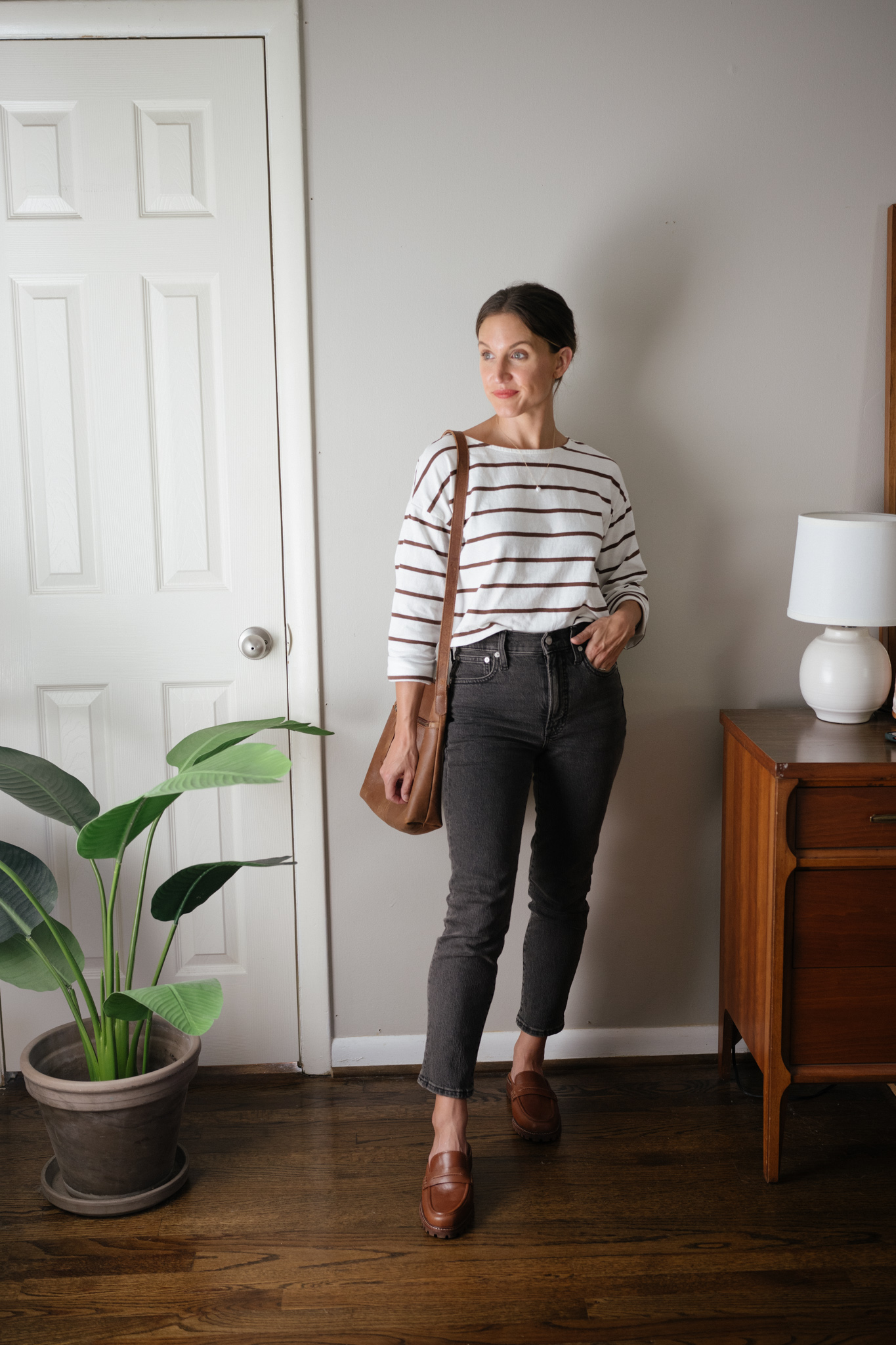 ashley wearing a cropped striped tee, washed black denim, brown loafers mules, and a brown leather crossbody bag