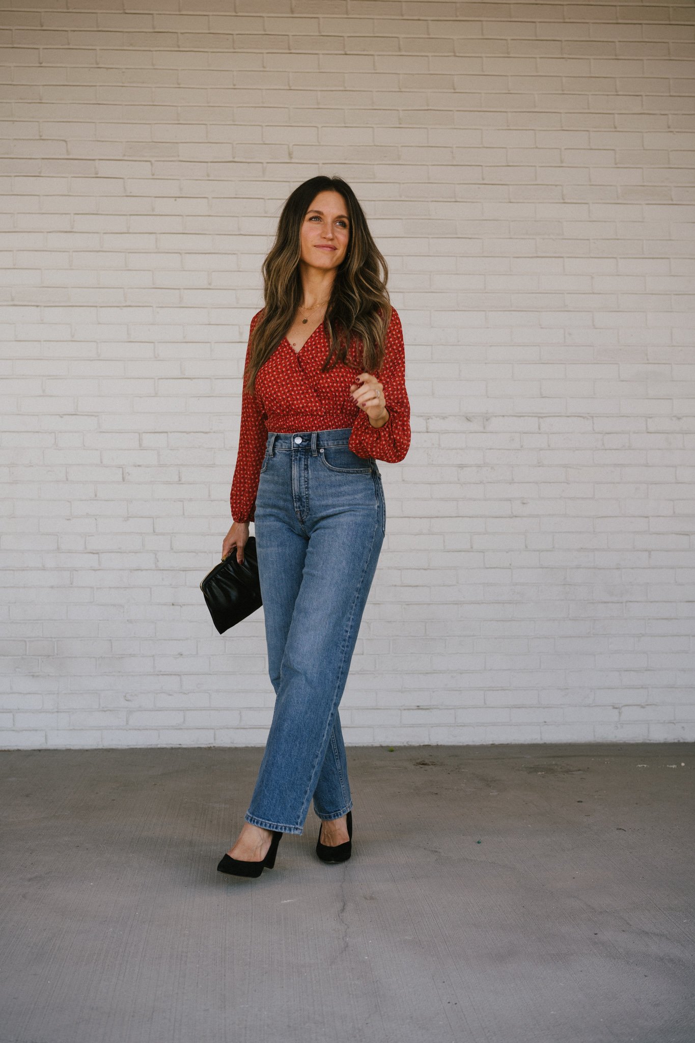 ashley wearing a fall floral blouse with denim, black pumps, and a black clutch bag