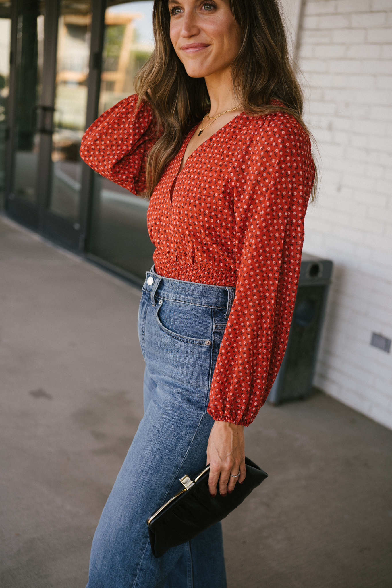 ashley wearing a fall floral blouse, blue denim standing in front of a white brick building