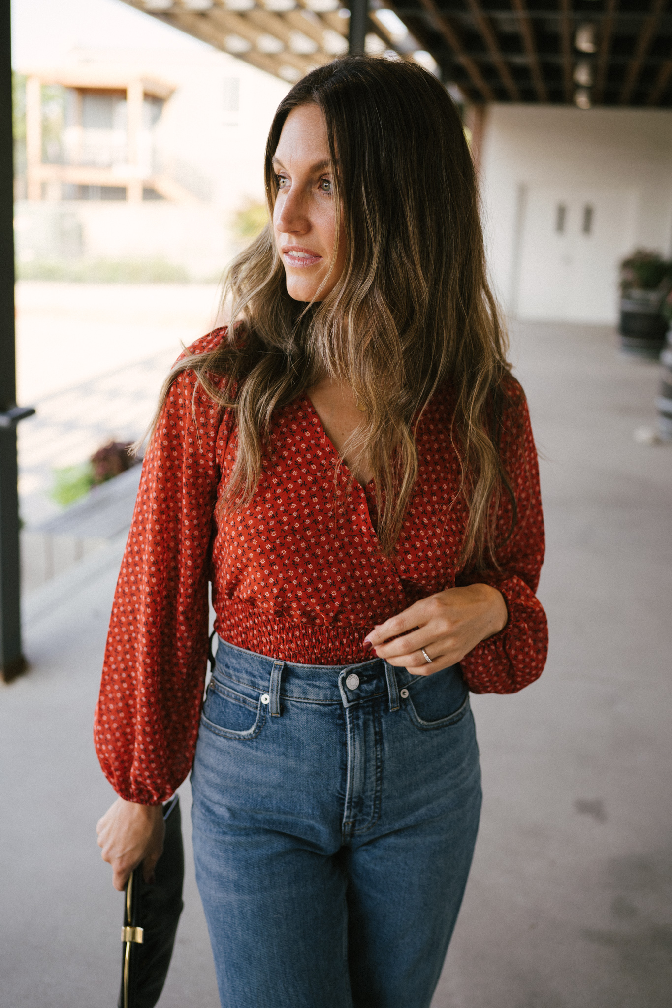 ashley wearing a fall floral blouse with denim, black pumps, and a black clutch bag