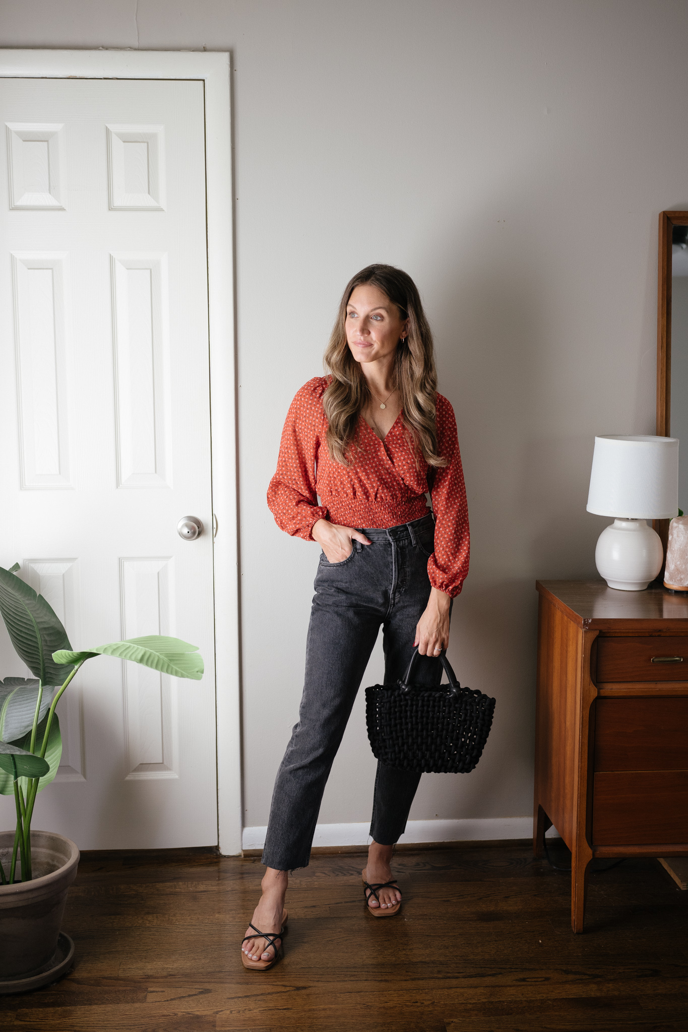 ashley wearing a red floral blouse, washed black denim, black strappy sandals, and a black woven bag