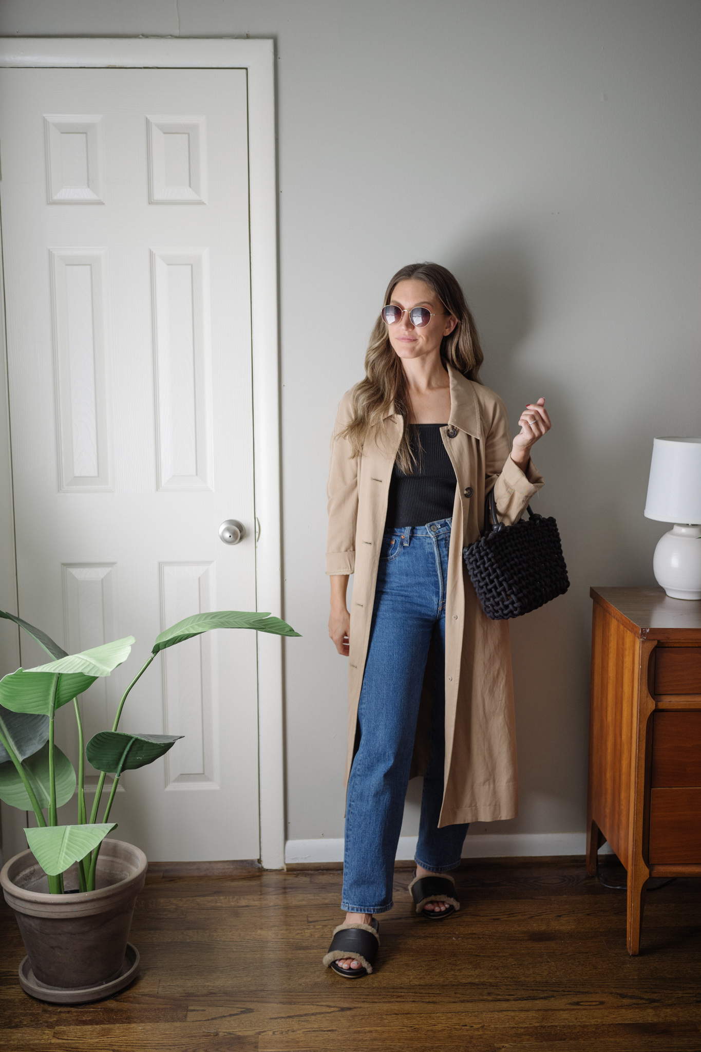 a neutral outfit for fall with a black sweater tank, straight denim, trench coat, and shearling slide sandals
