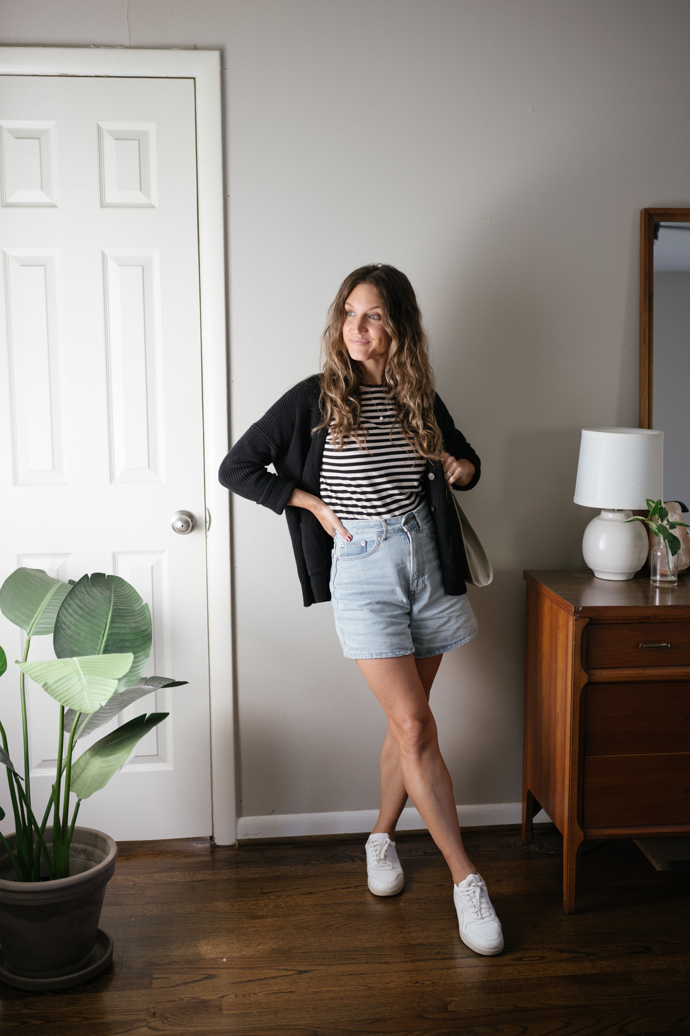 a neutral outfit for fall with a striped tee, black cardigan, light wash denim shorts, and white sneakers