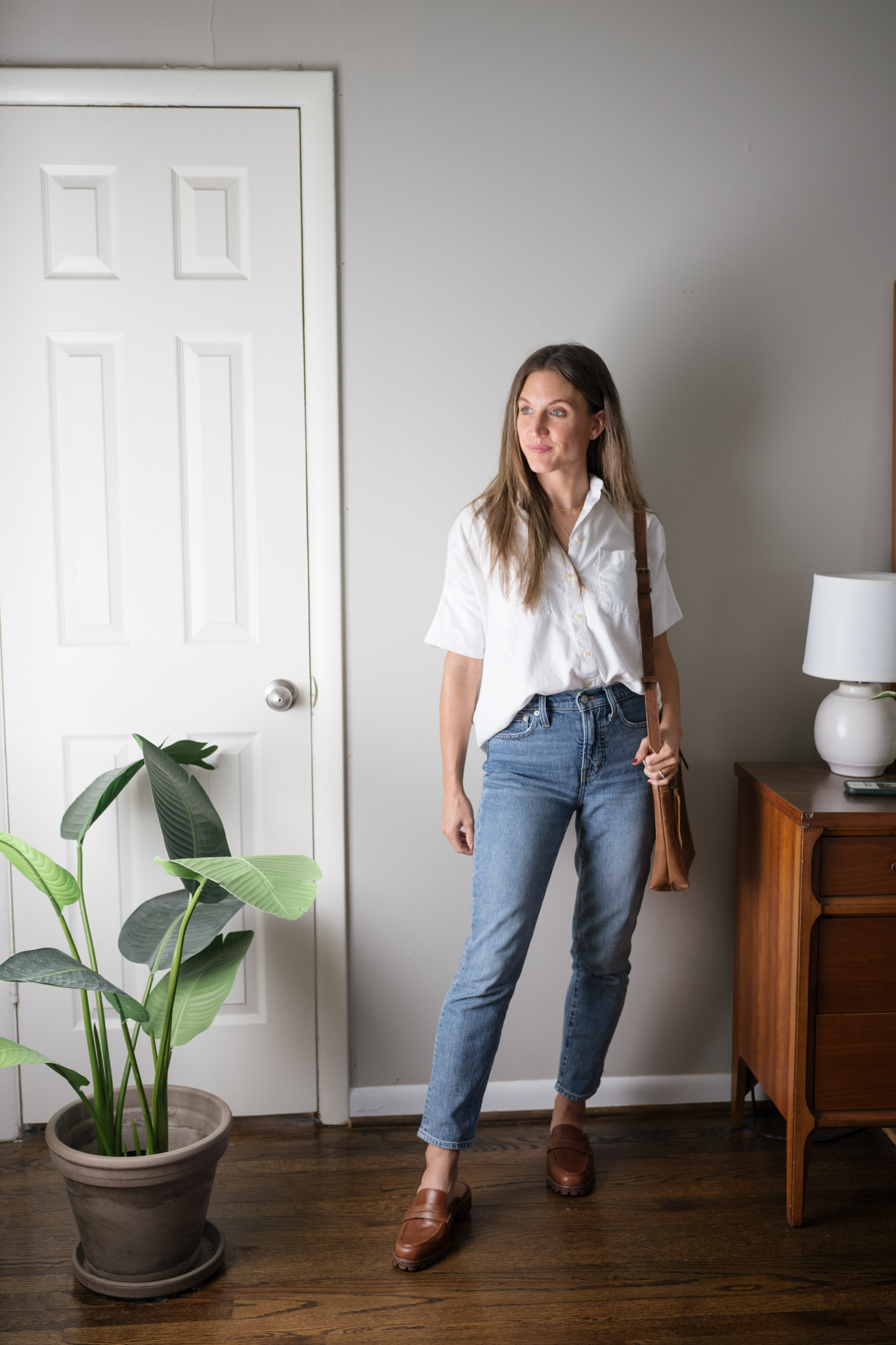 a neutral outfit for fall with a short sleeved white button down, mid-wash denim, and brown loafer mules
