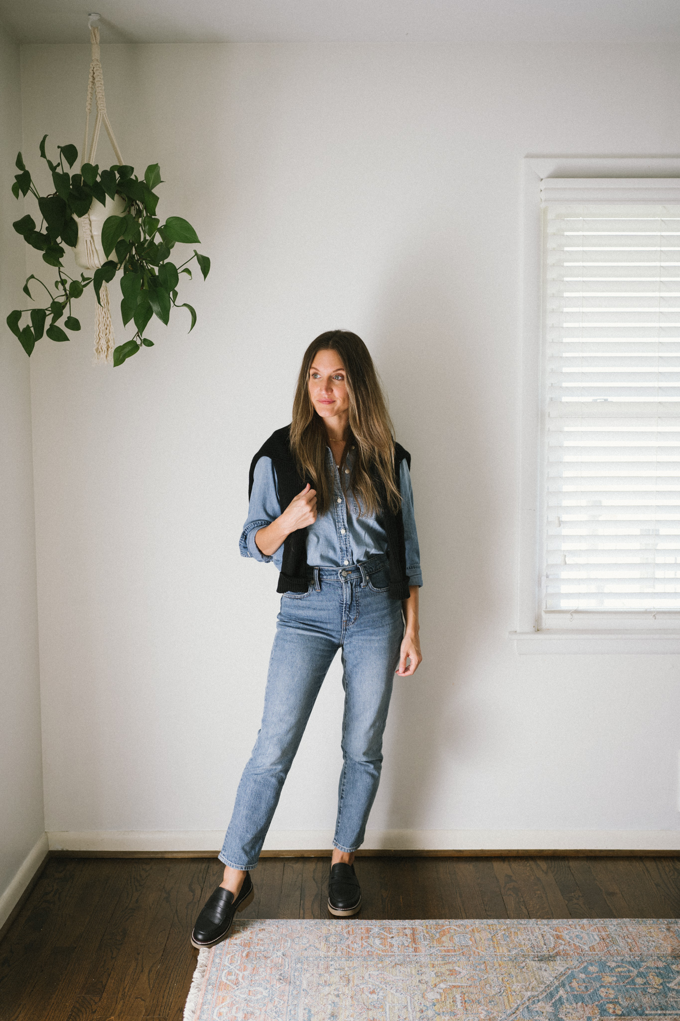 a denim on denim look with a sweater worn over the shoulders and black loafers