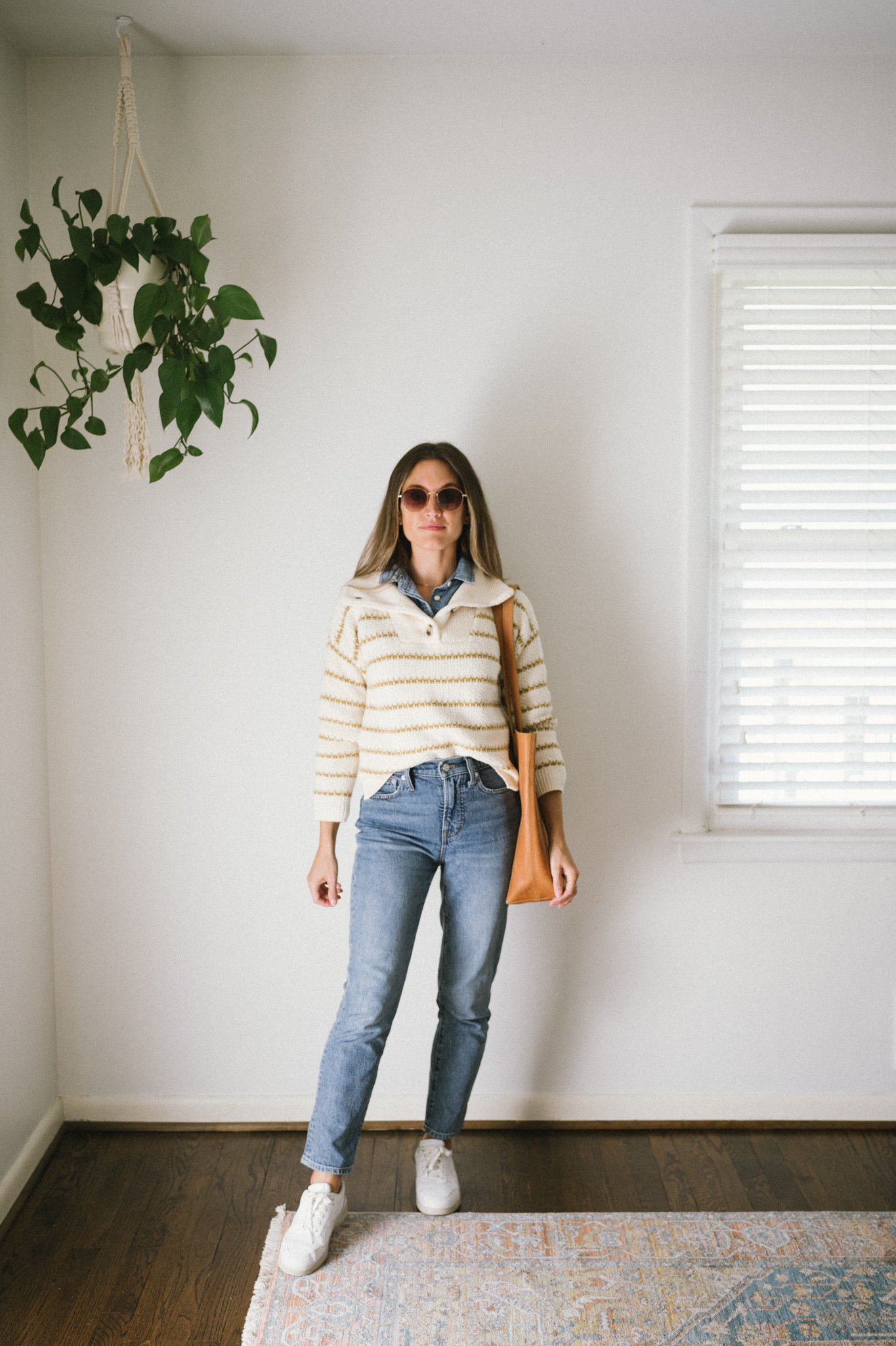 a denim on denim look with a collared sweater worn over a denim top with denim blue jeans and white sneakers