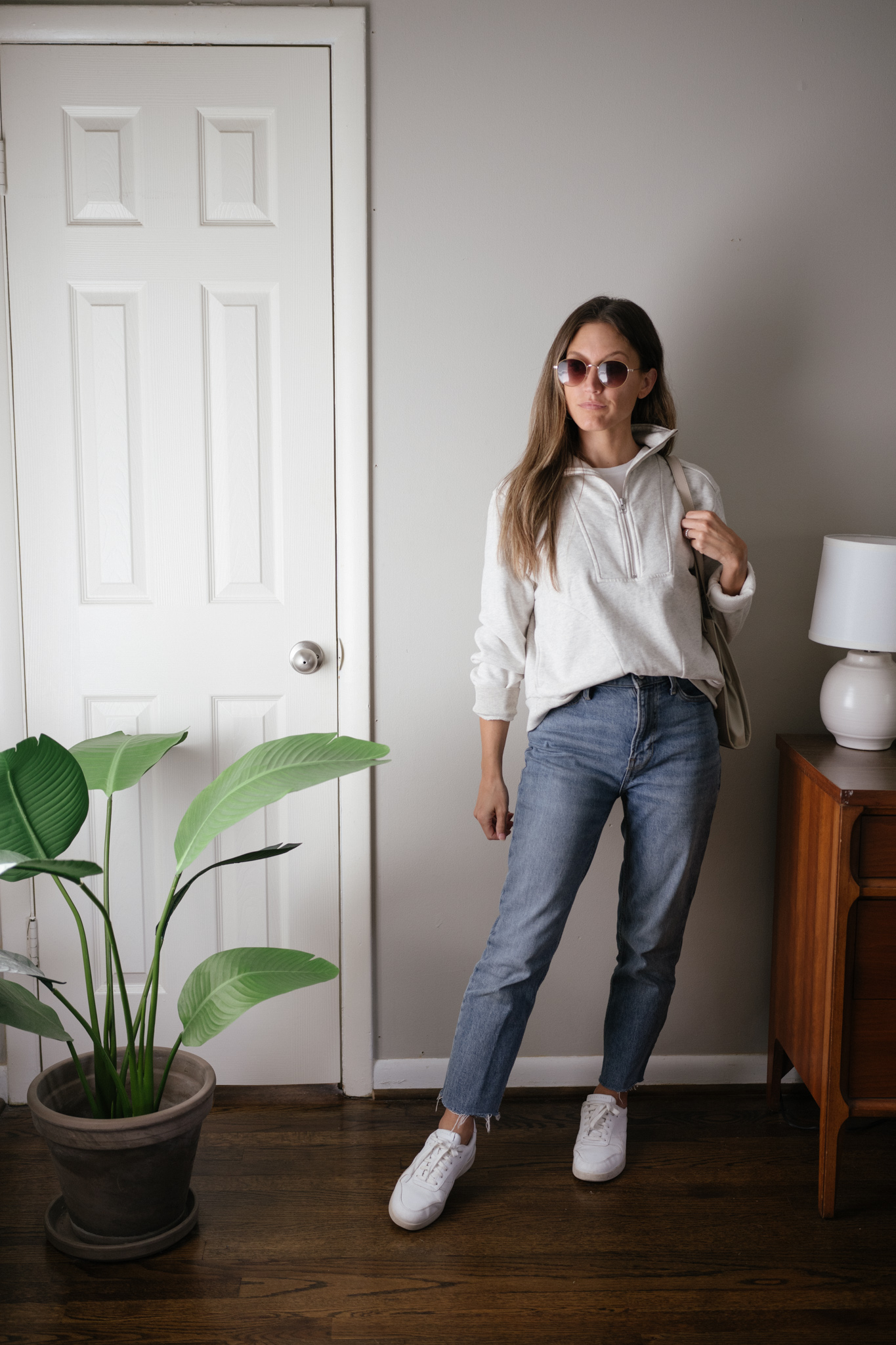 a neutral outfit for fall with a gray half zip sweatshirt, mid-wash denim, and white sneakers
