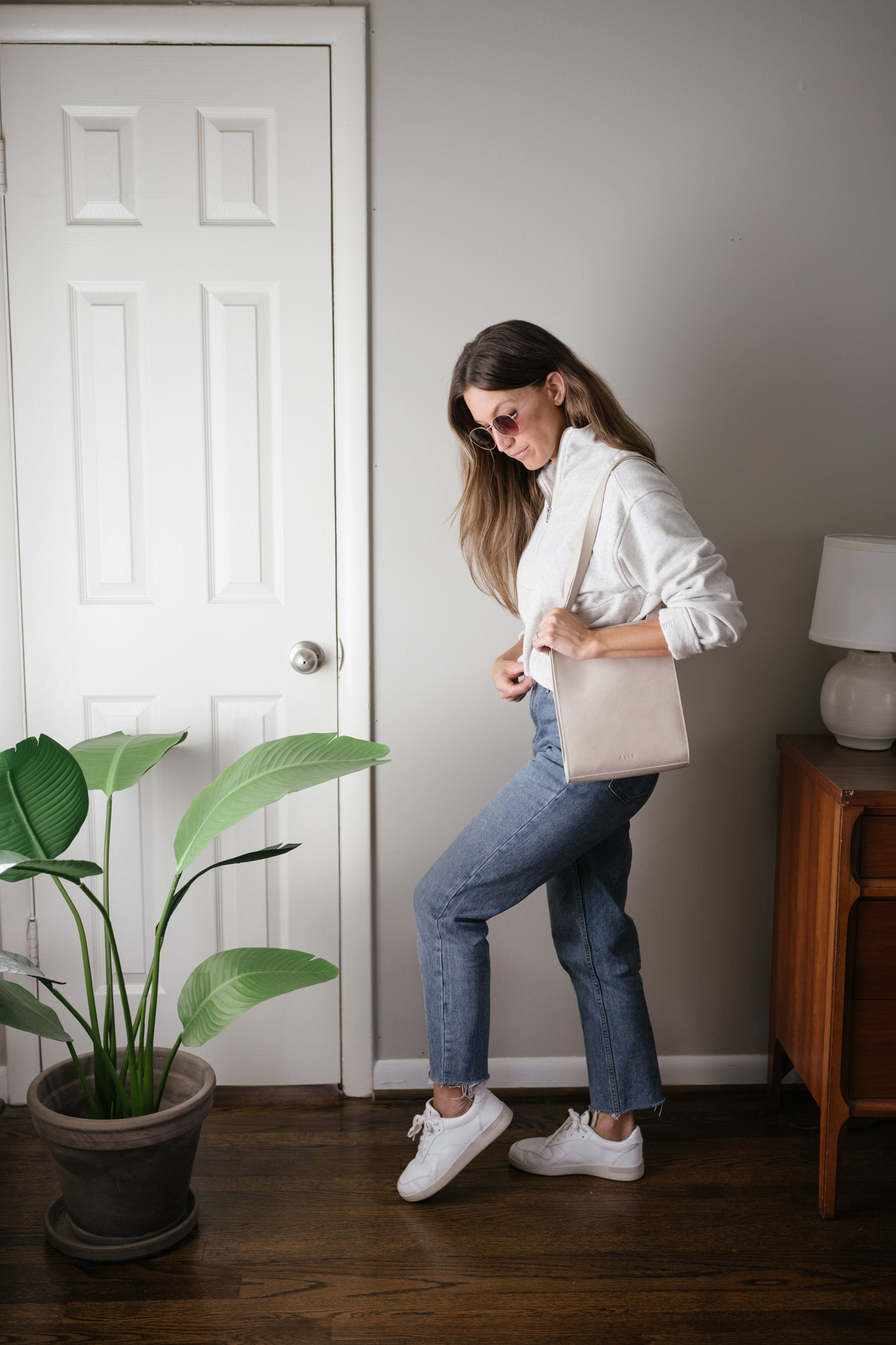 a neutral outfit for fall with a gray half zip sweatshirt, mid-wash denim, and white sneakers