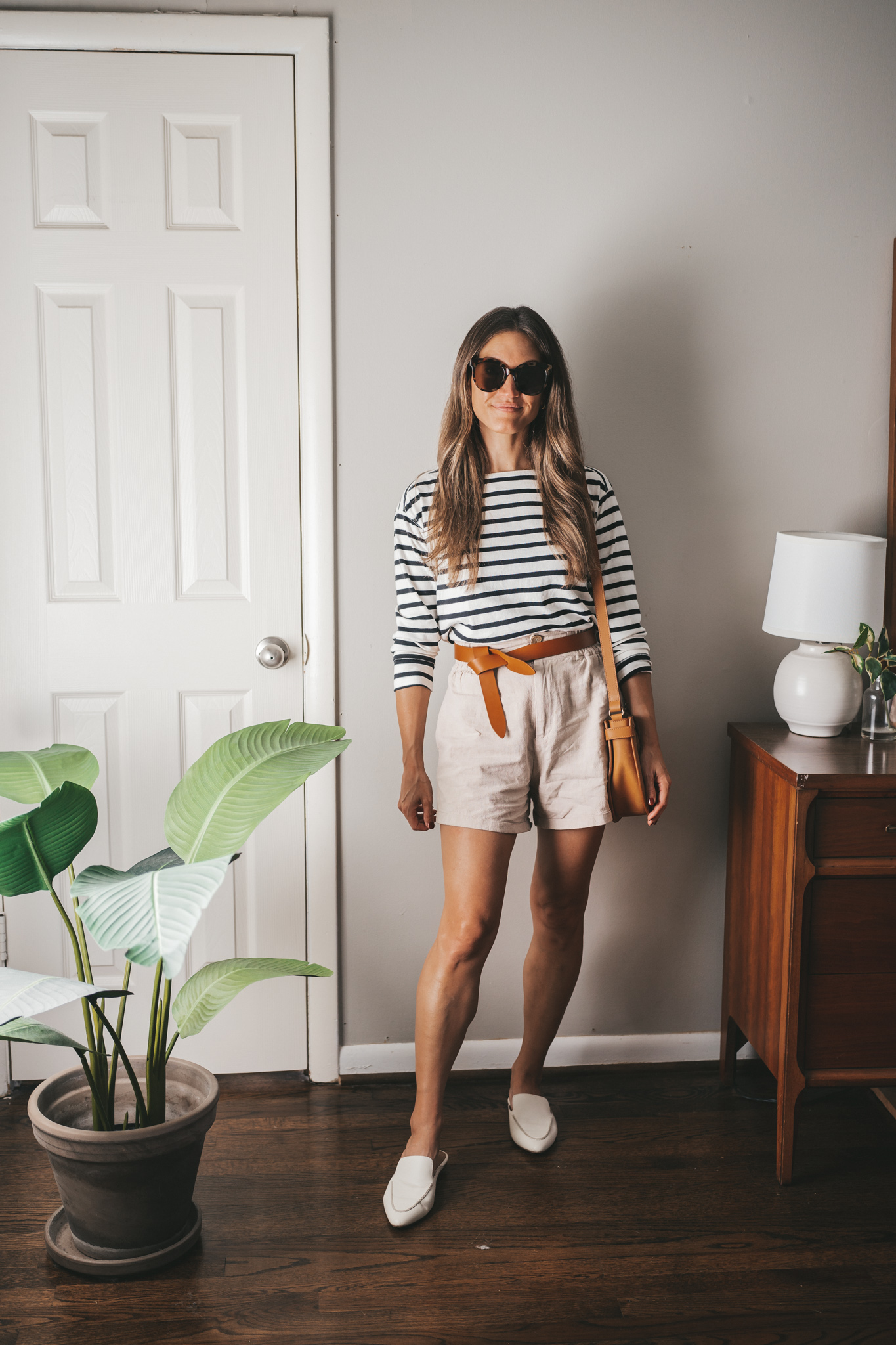 an early fall outfit with a striped top, linen shorts, white mules, and a cognac tie belt