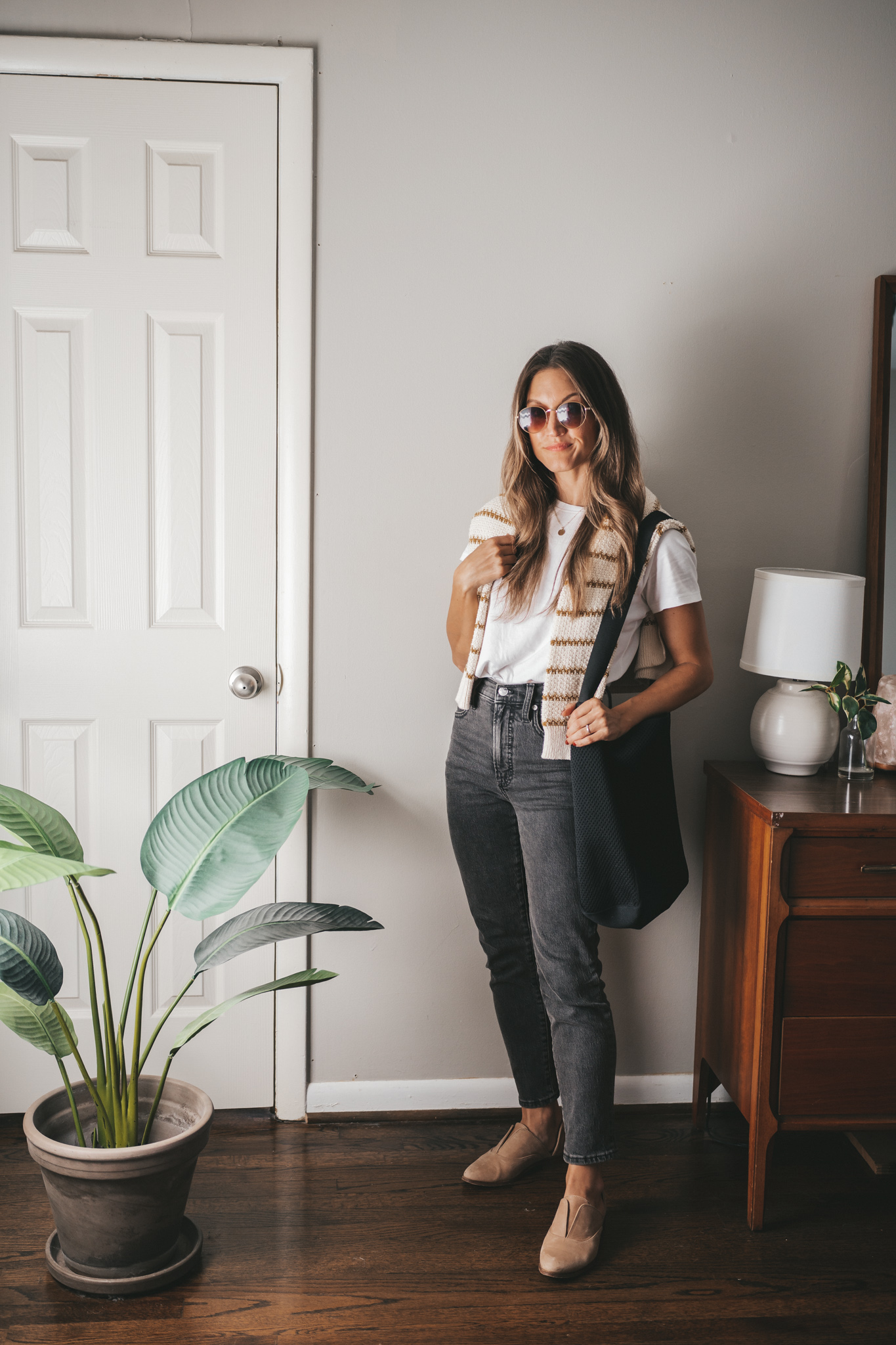 a fall outfit with a white tee, striped sweater worn over the shoulders, black denim, and nude oxfords