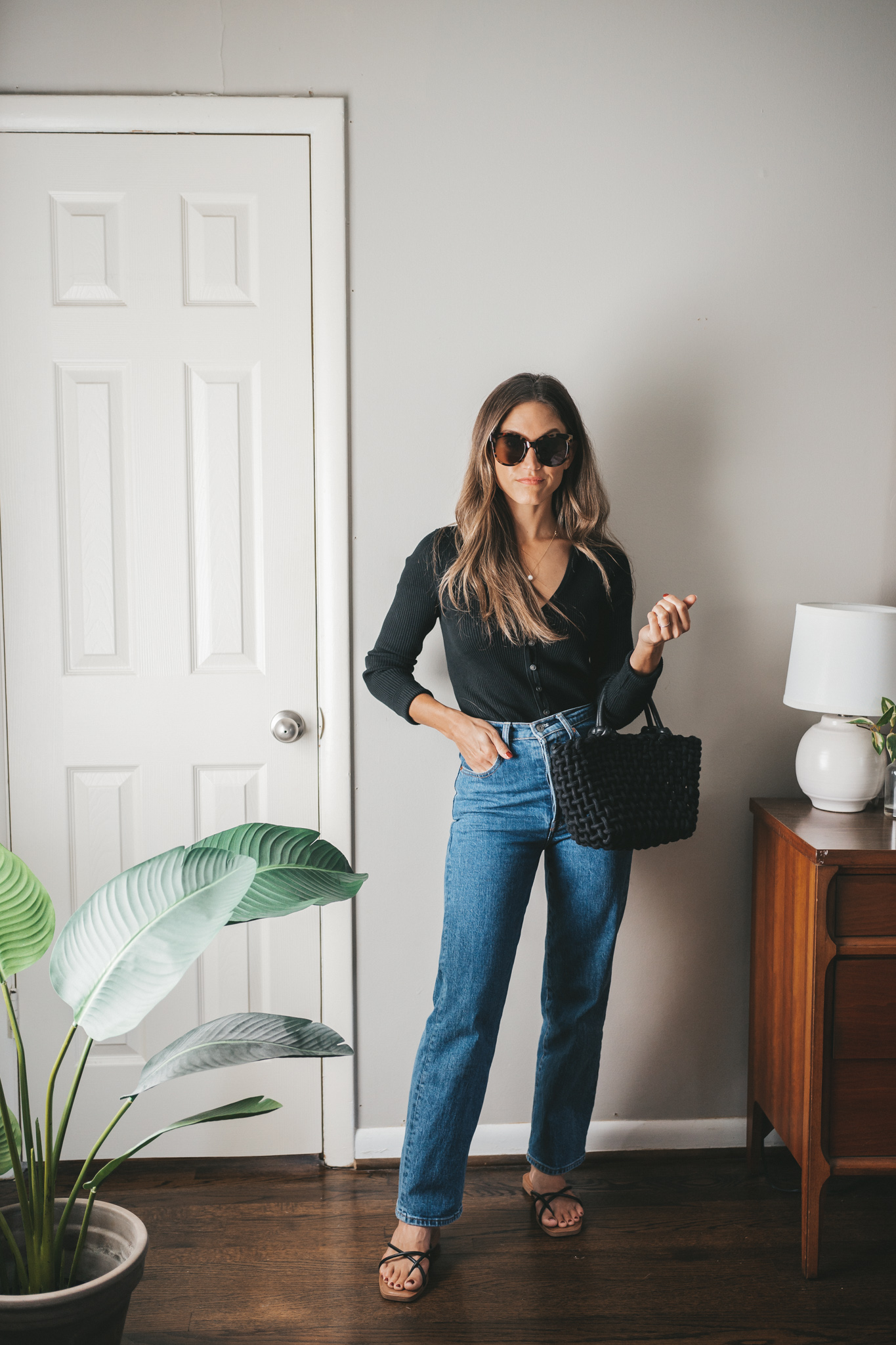 an early fall outfit with a cropped black cardigan, midwash high waisted jeans, and black strappy sandals