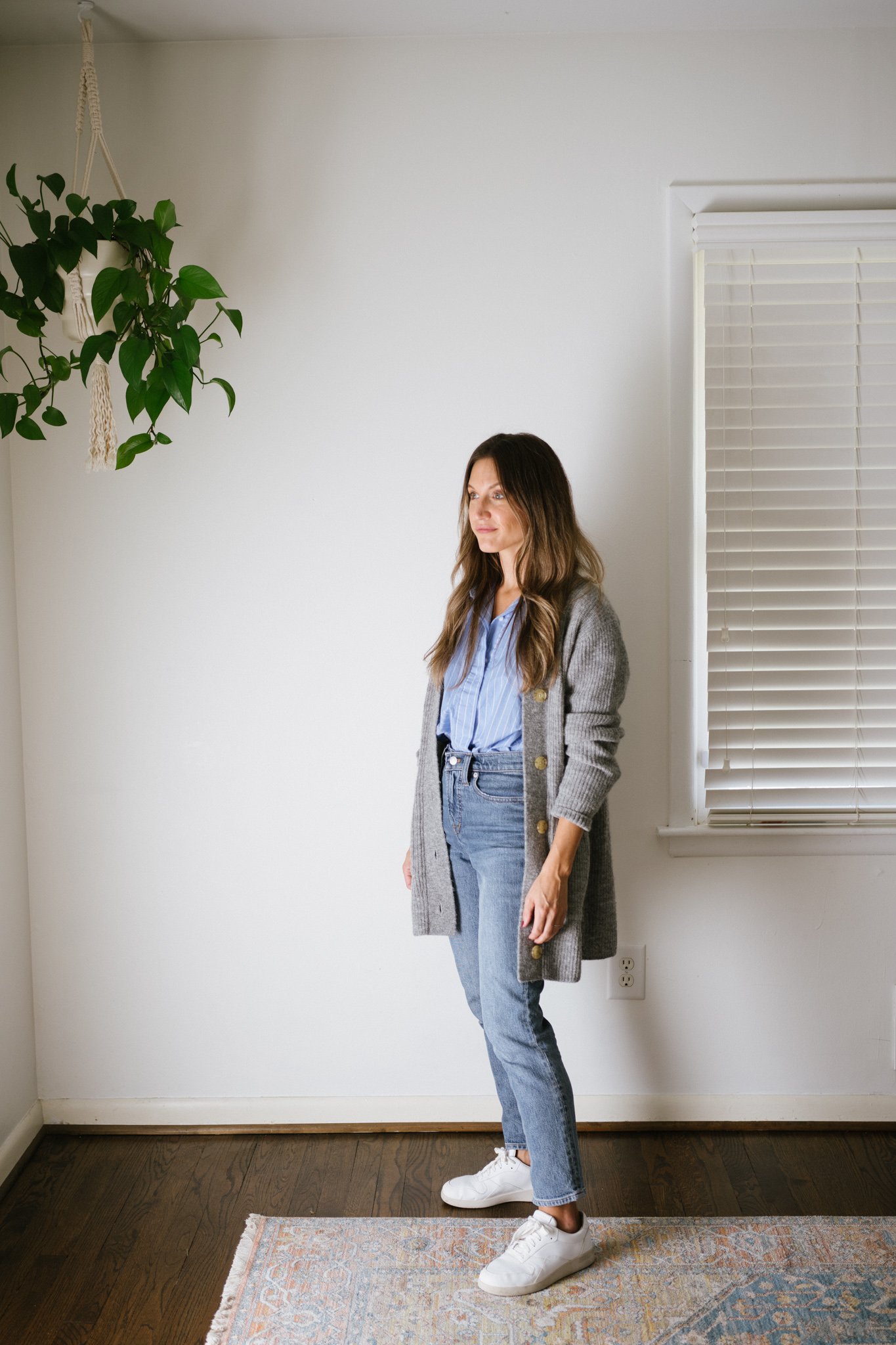 a classic fall outfit with a blue button down, gray cardigan, mid-wash denim, and white sneakers