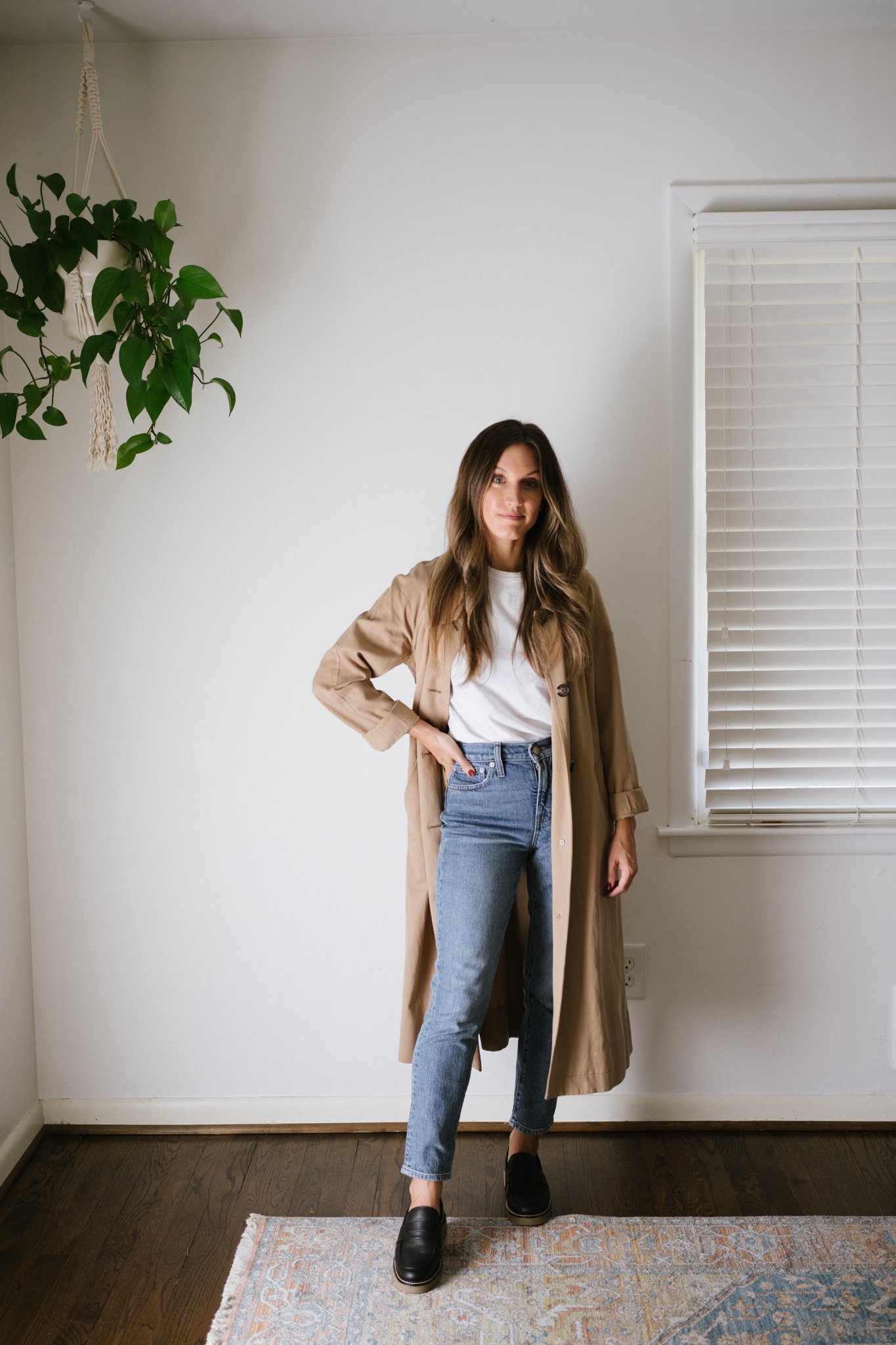 a minimalist fall outfit with a white tee, tan trench coat, mid-wash denim, and black loafers