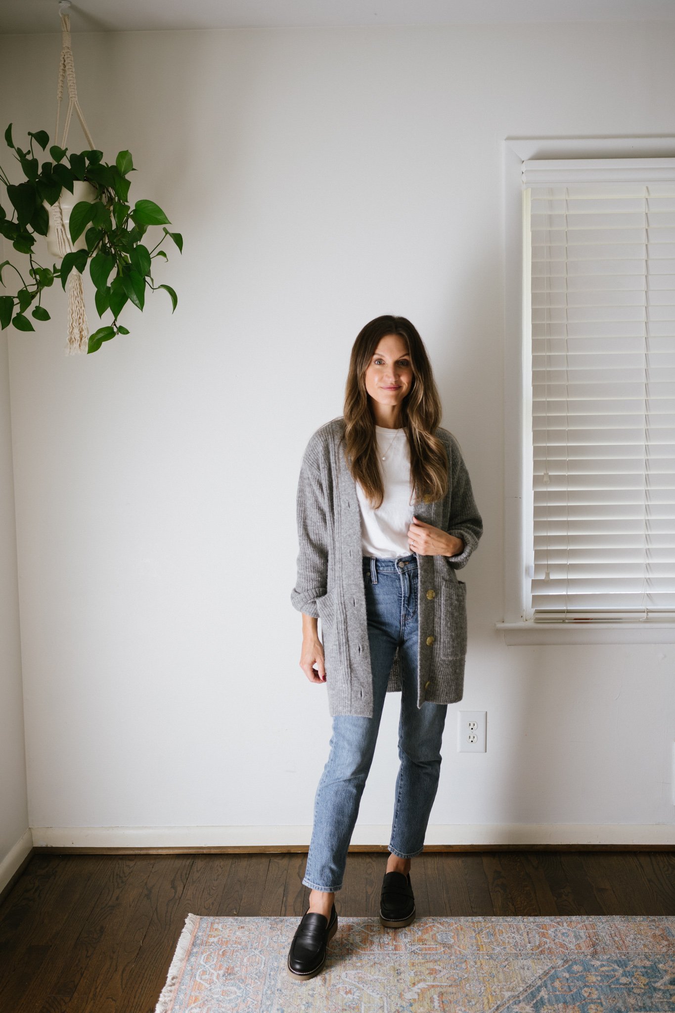 a minimalist fall outfit with a white tee, gray cardigan, mid-wash denim, and black loafers