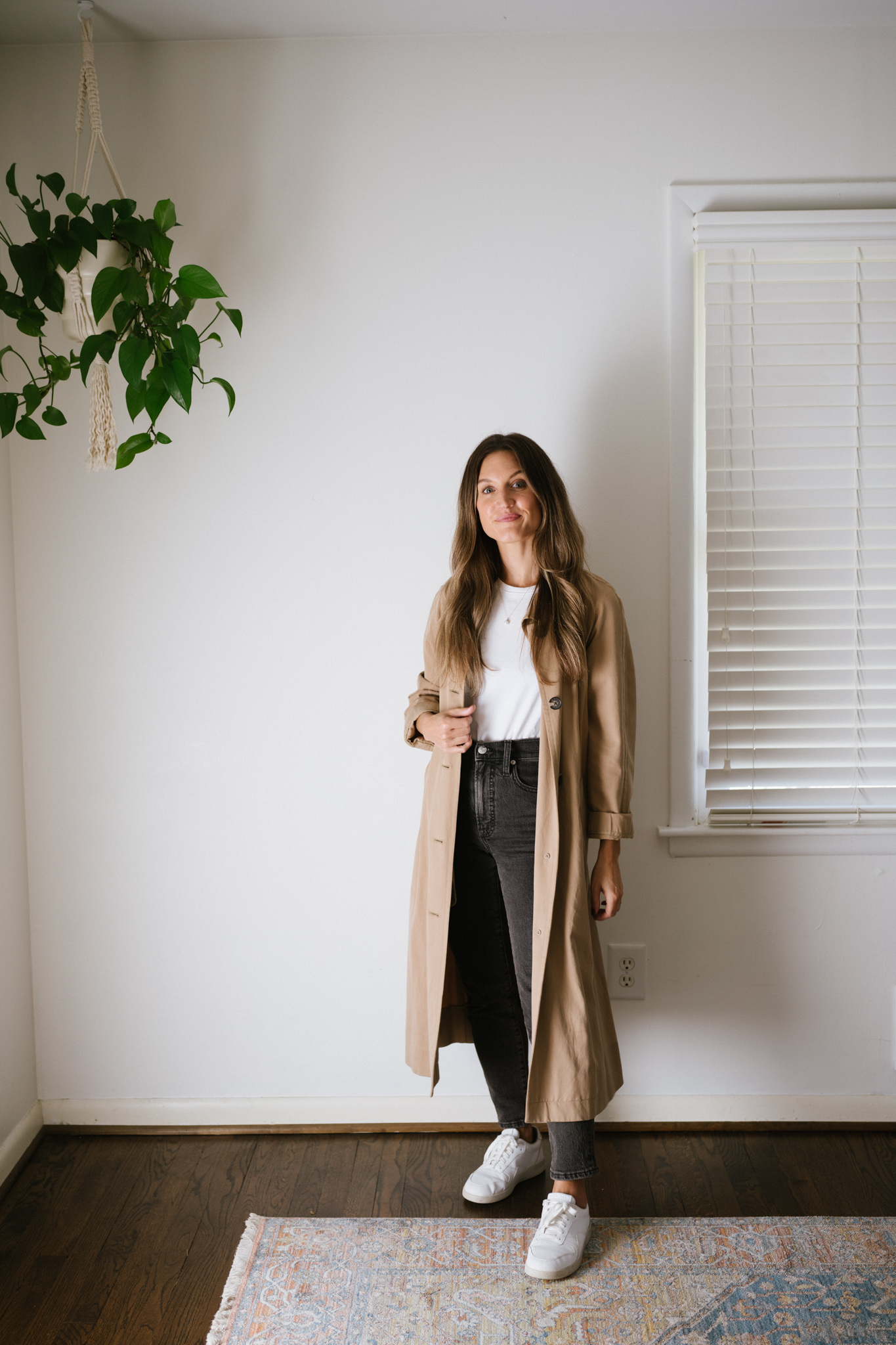 a minimalist outfit with a white tee, tan trench coat, black denim, and white sneakers