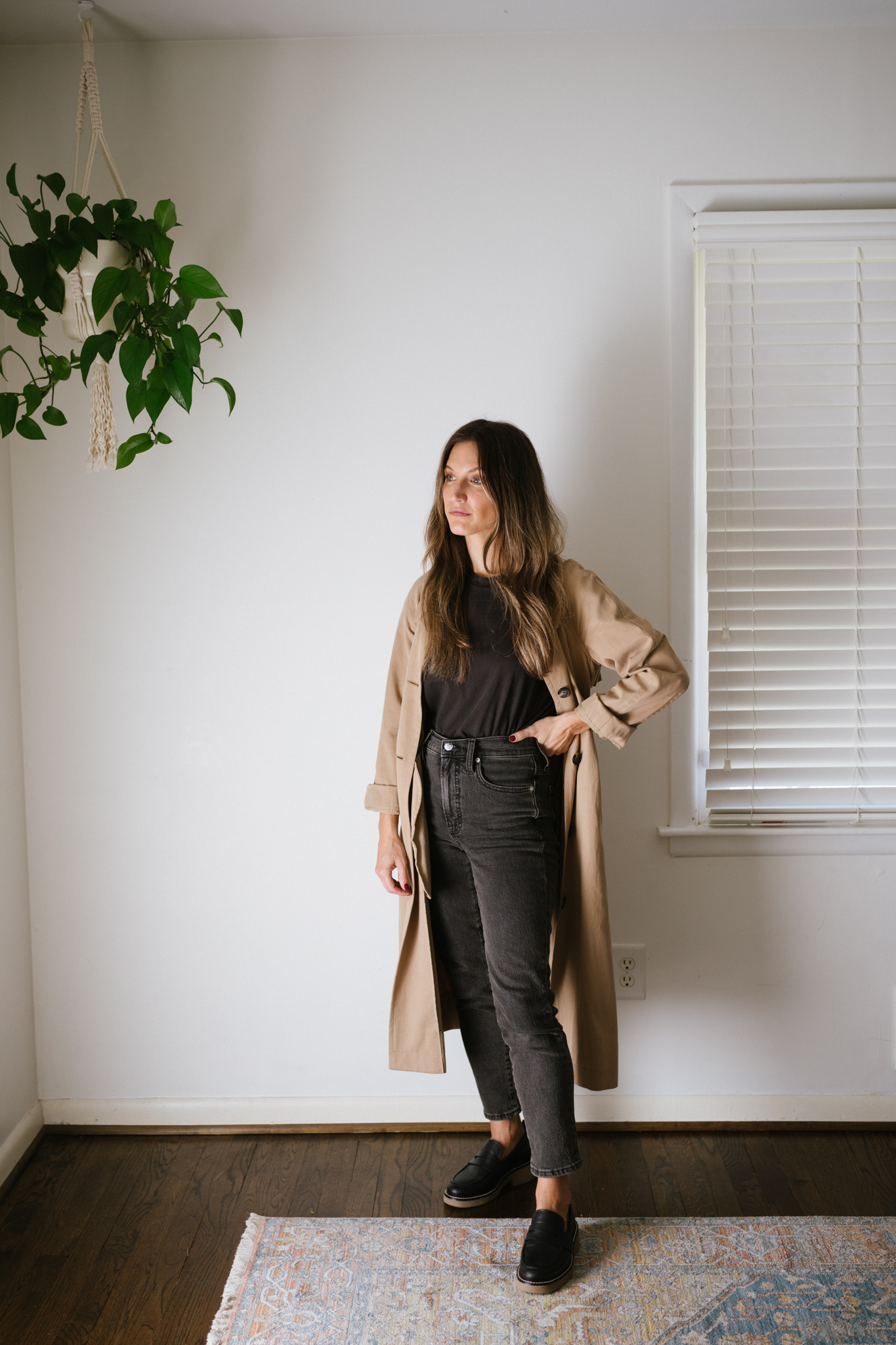 a minimalist outfit for fall with a black tee, tan trench coat, black denim, and black loafers
