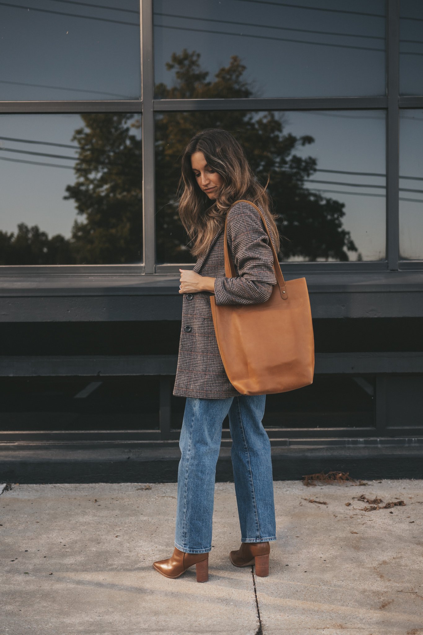 a plaid blazer outfit with a white tee, straight denim, brown ankle boots, and a cognac leather tote bag