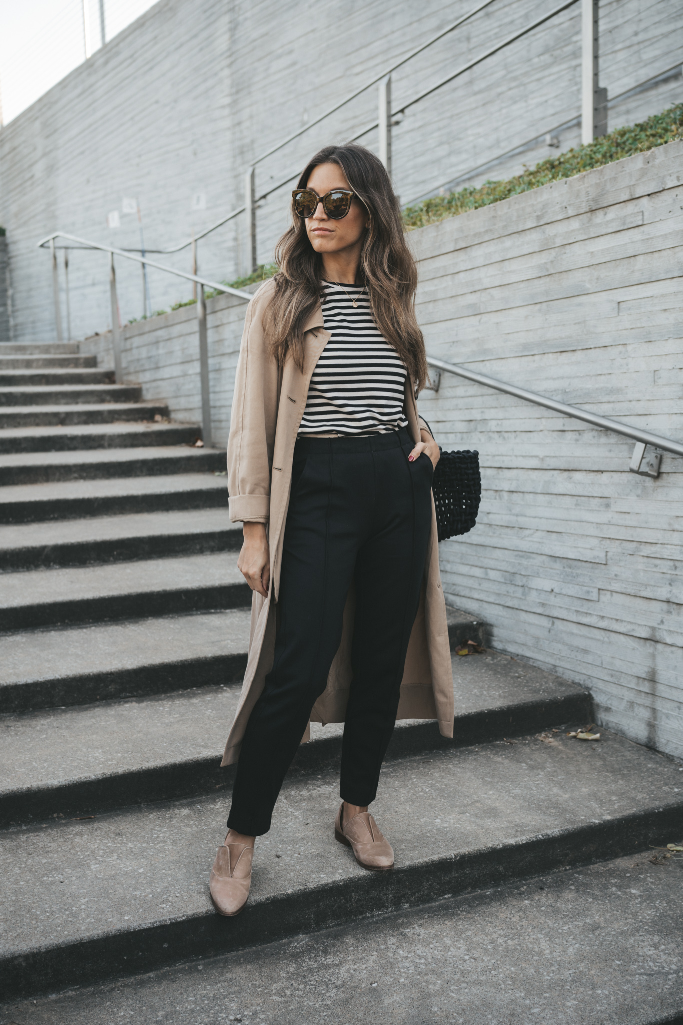 ashley wearing the Everlane Dream pant paired with a striped tee, tan trench coat, nude Oxfords, and a black woven bag