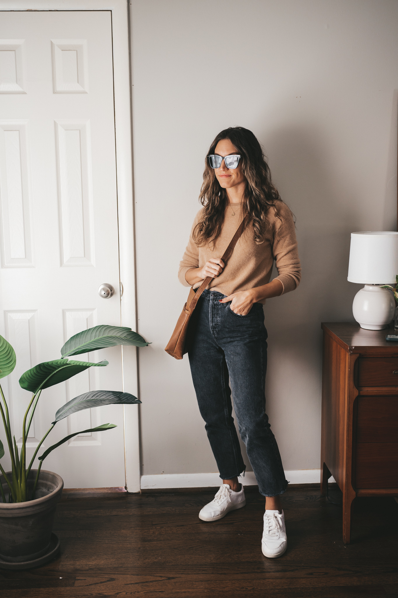 casual outfit with a camel cashmere sweater, black denim, and white sneakers