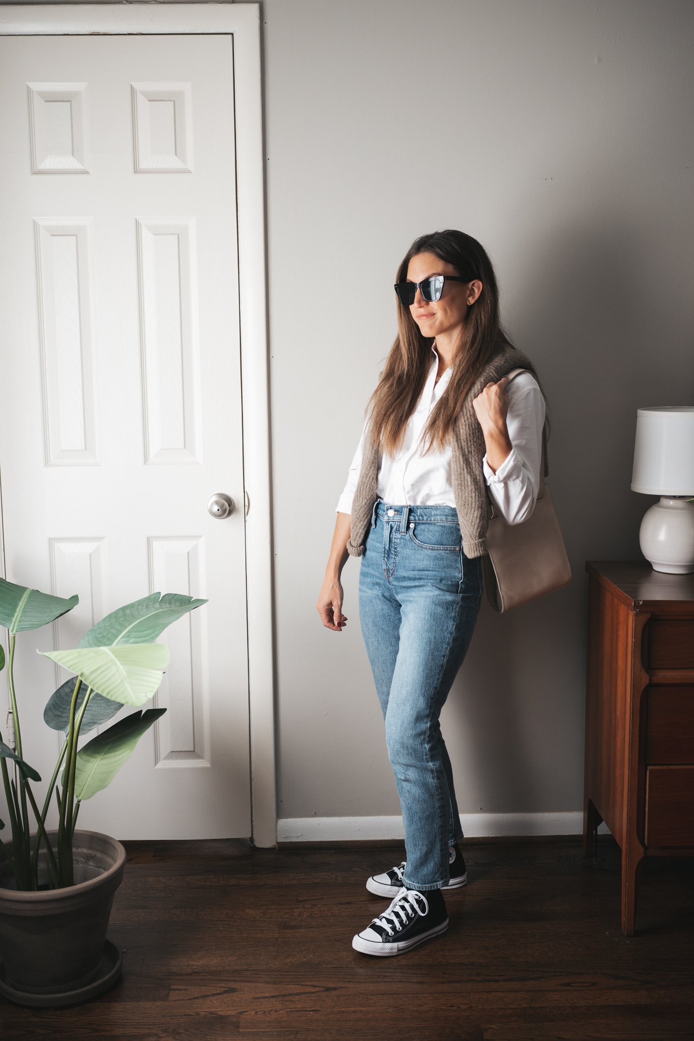 fall outfit with denim, a white button down, sweater over the shoulders and high top Converse