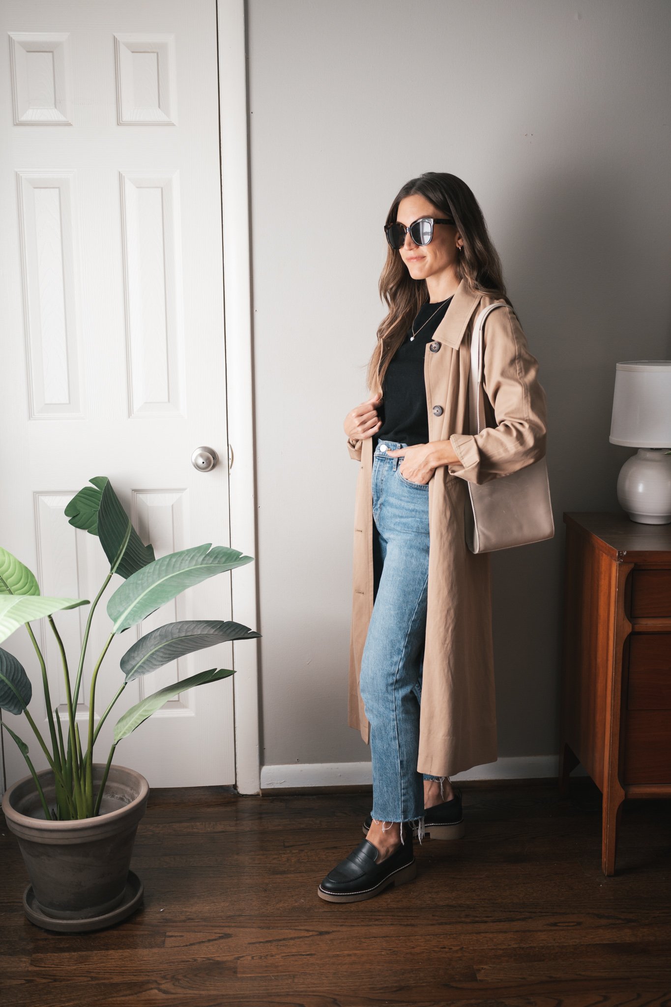 minimalist fall outfit idea with a black sweater, trench coat, medium wash denim, and black loafers